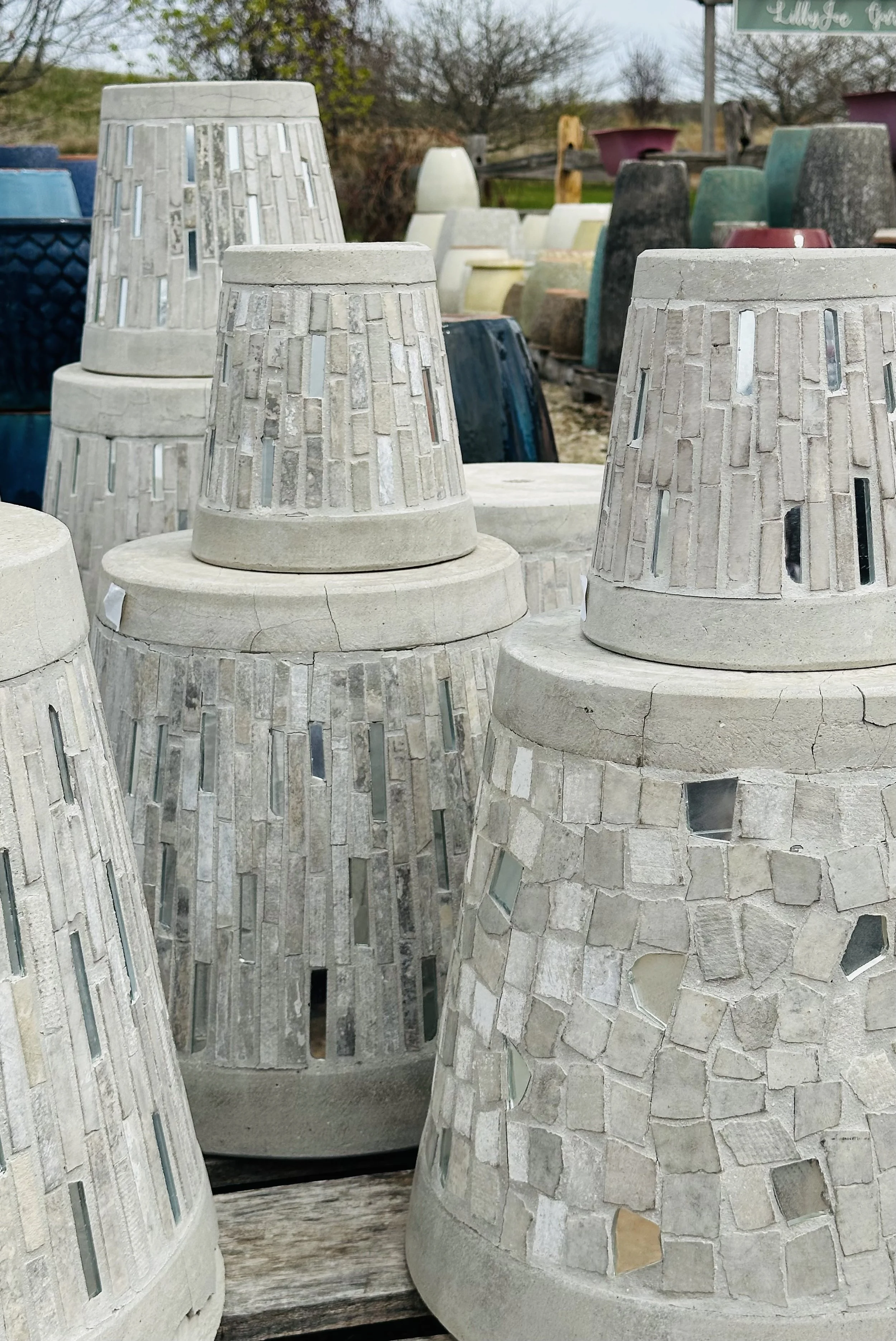 Concrete garden lamps with mosaic designs displayed outdoors at a nursery or garden center.