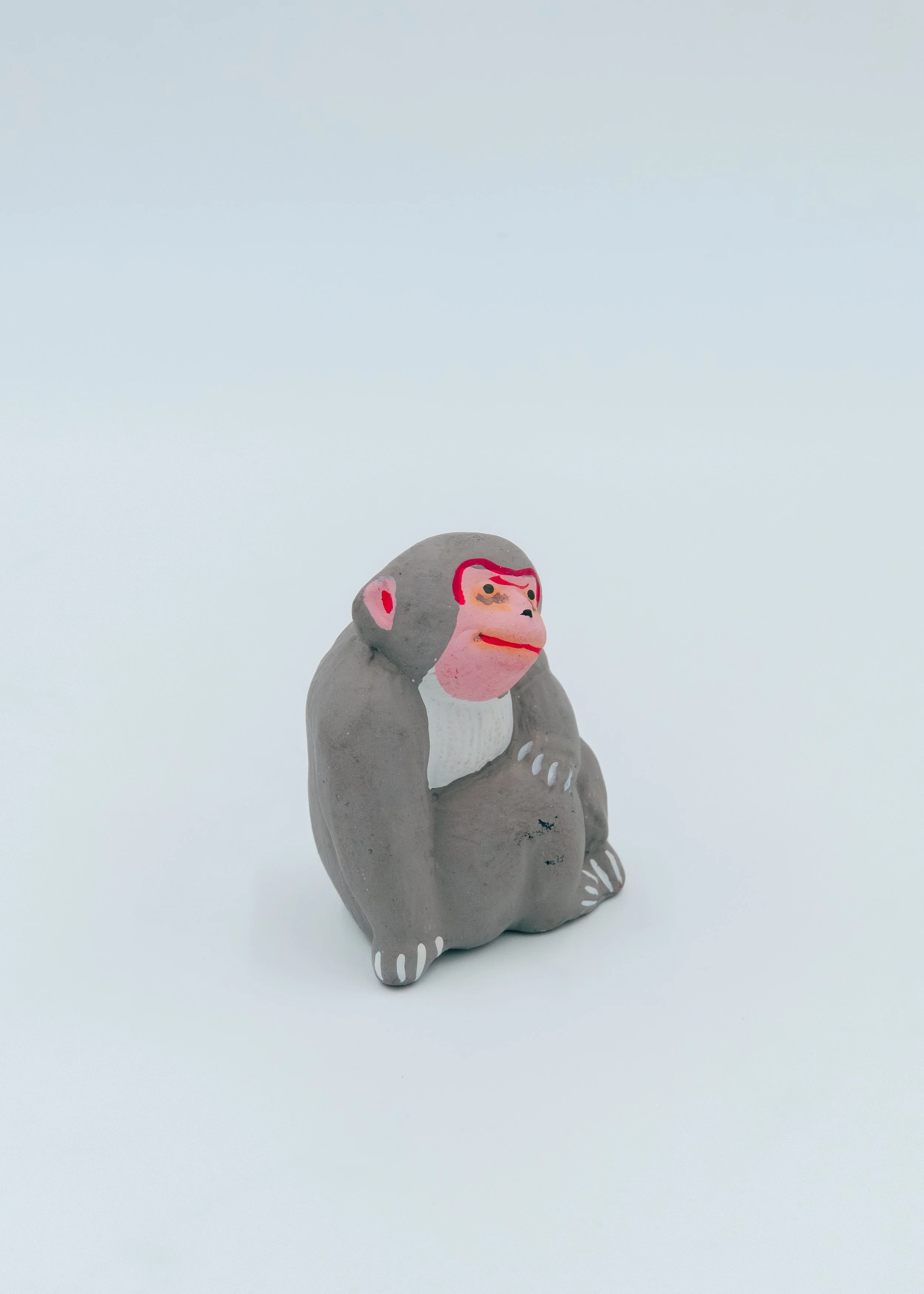 Vintage grey Japanese monkey spirit mascot "Masaru" seated in a traditional protective huddle posture, featuring a vibrant hand-painted red face.