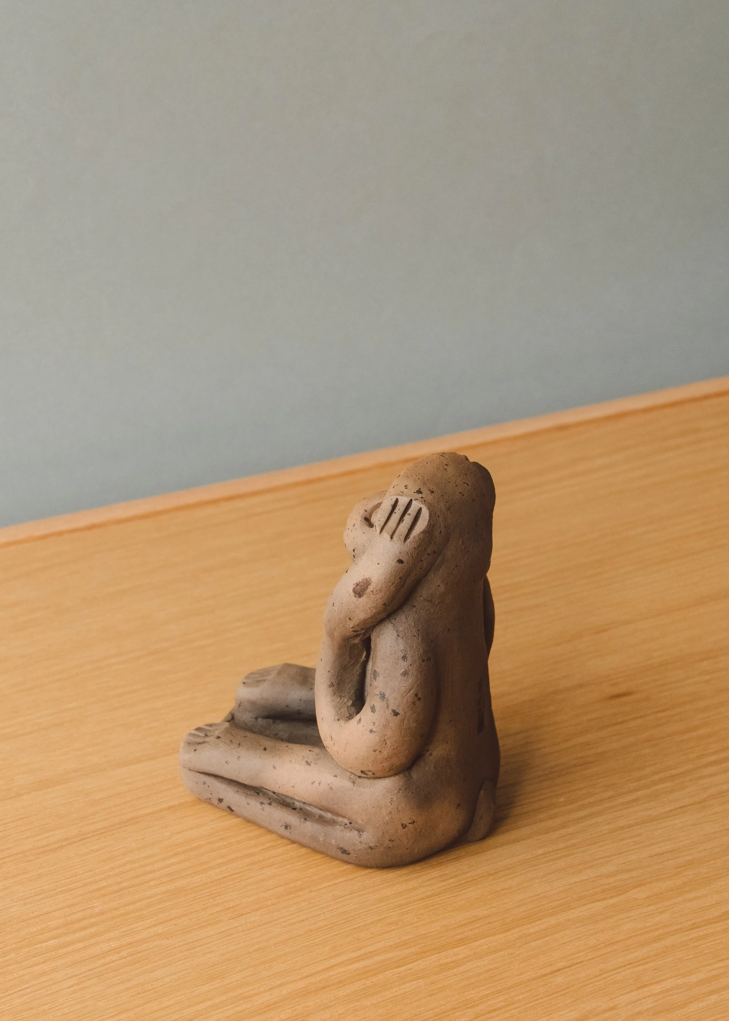 Side angle of a hand-molded "Hear No Evil" earthenware simian sculpture. Unglazed red clay retaining the smoke-stained patina from a 1,300-year-old traditional Japanese kiln process.