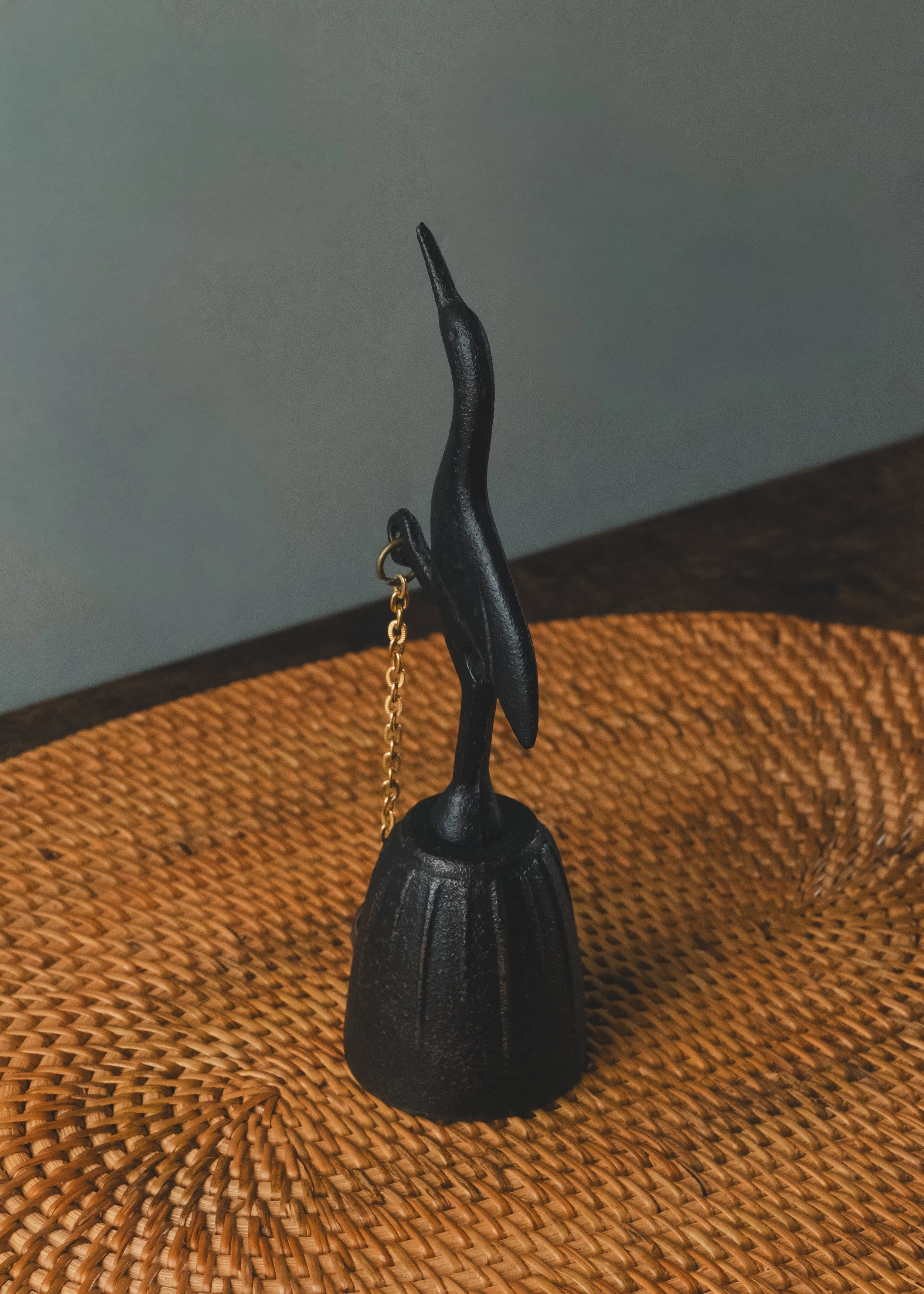 Nambu Tekki iron crane table bell silhouette on a woven surface. Traditional Japanese cast iron bell from the 1970s, designed for spatial purification and minimalist decor.