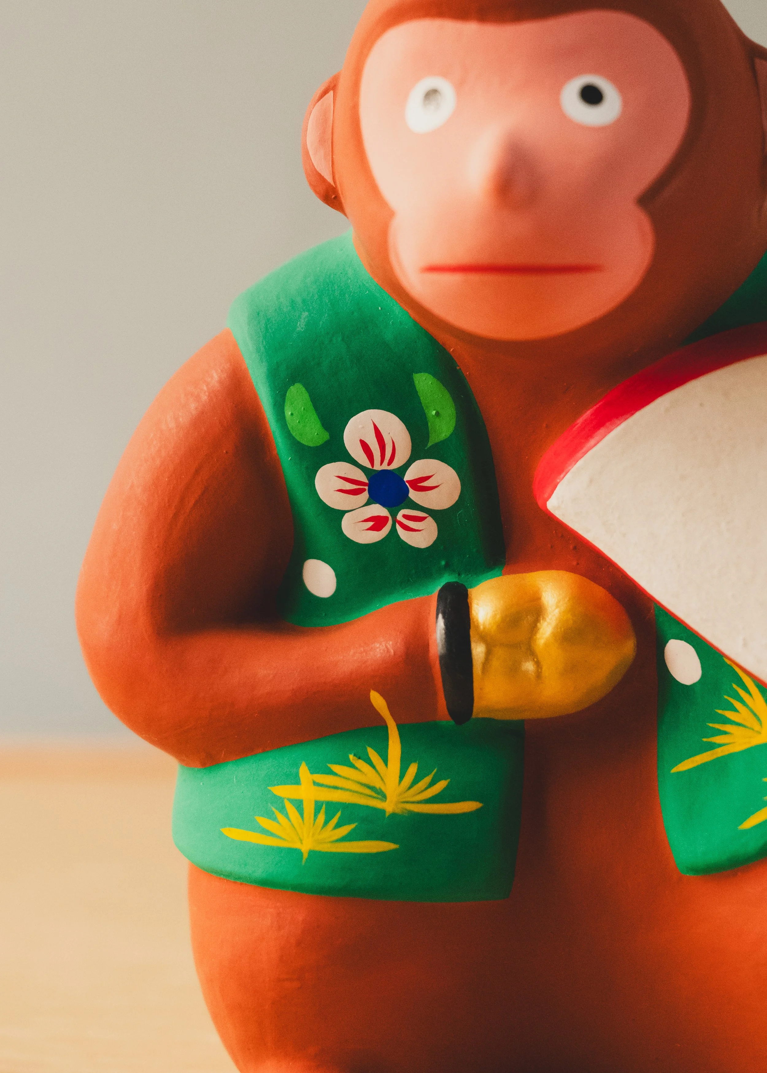 Macro detail of traditional hand-painted floral motifs on a Japanese clay monkey figurine. Evidence of the human touch in Mid-Century folk art.