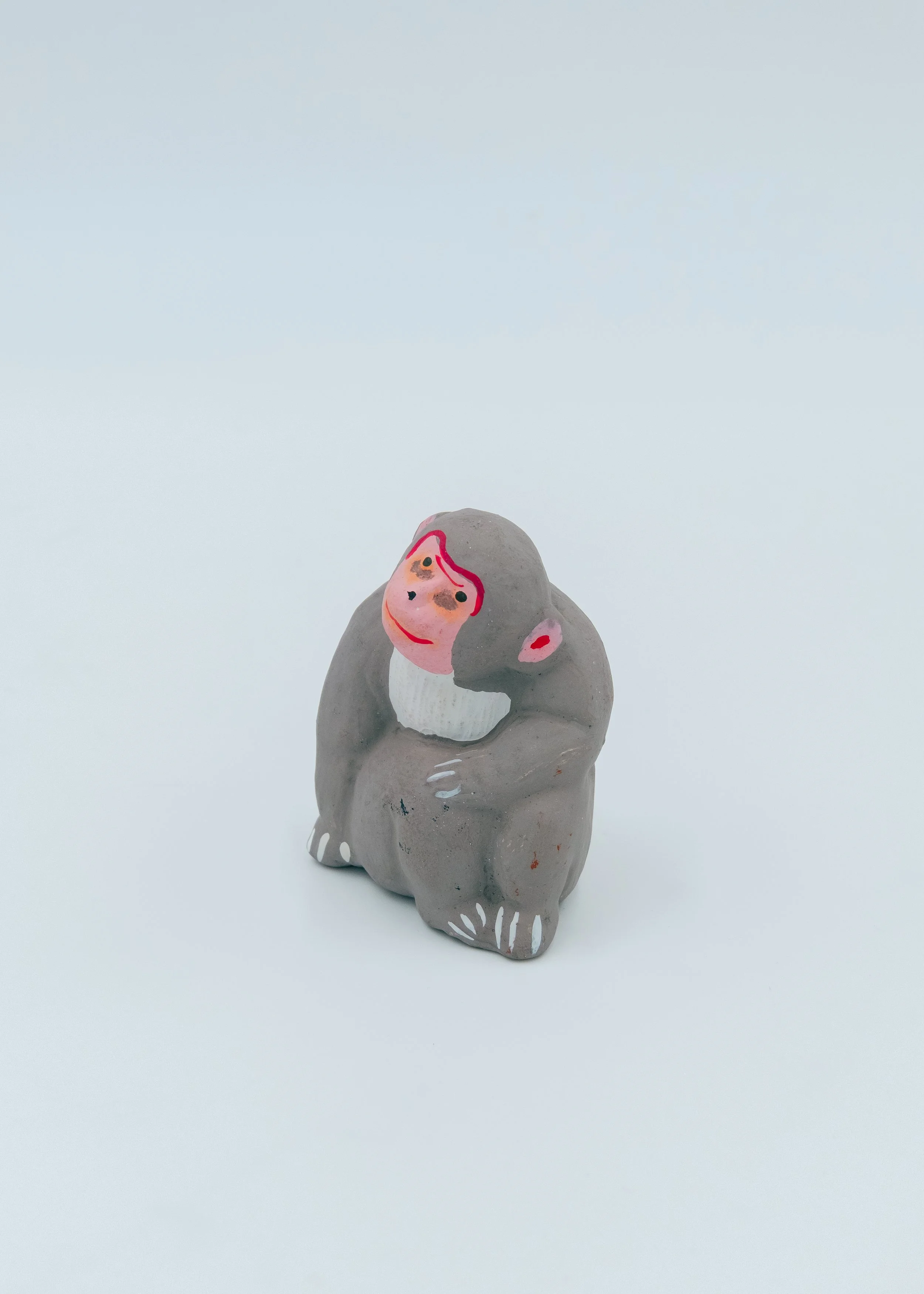 Vintage grey Japanese monkey spirit mascot "Masaru" seated in a traditional protective huddle posture, featuring a vibrant hand-painted red face.