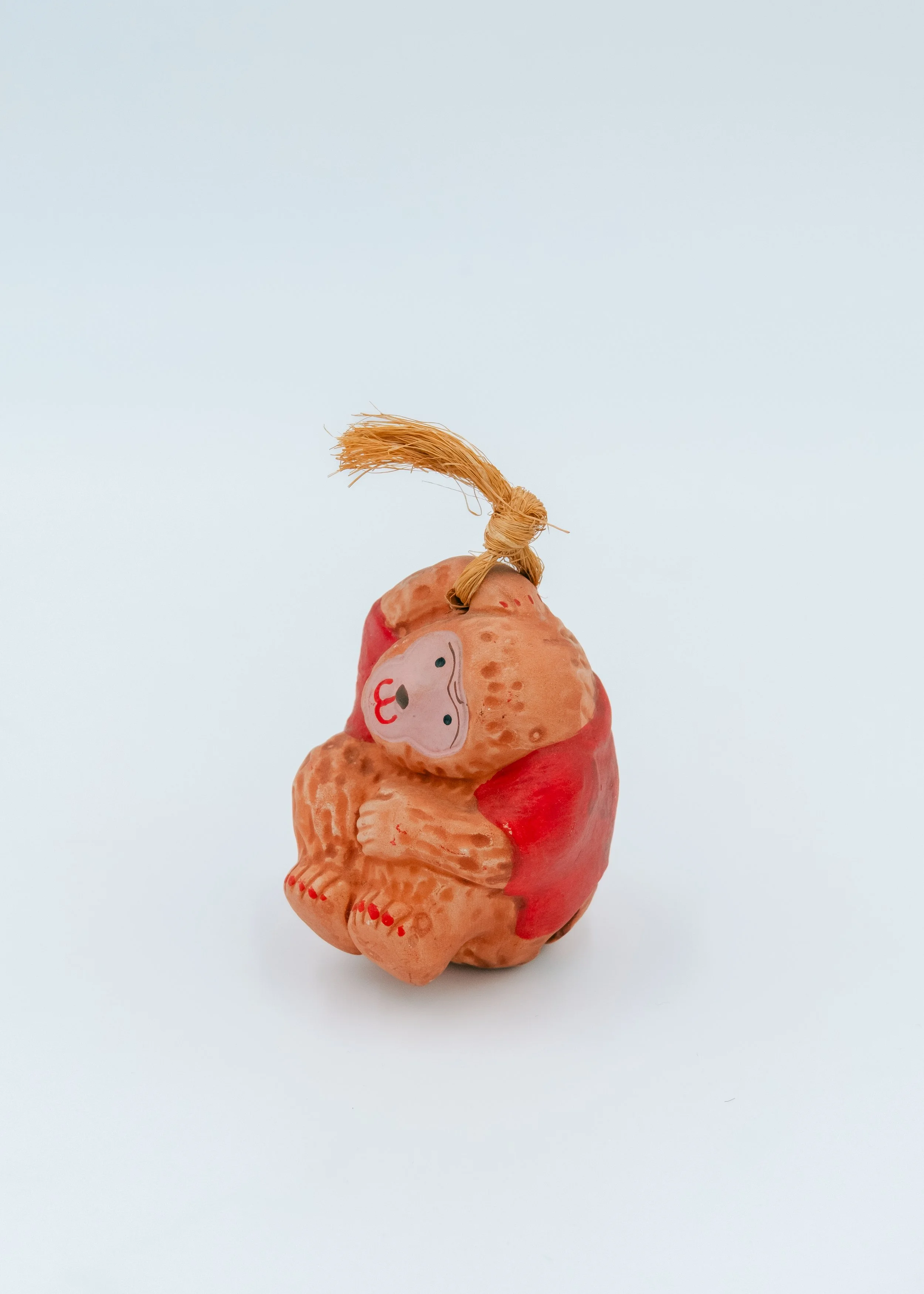 Vintage Japanese clay monkey bell mascot from Saga, wearing a vibrant scarlet hand-painted vest and jute cord, a symbolic amulet for warding off misfortune.