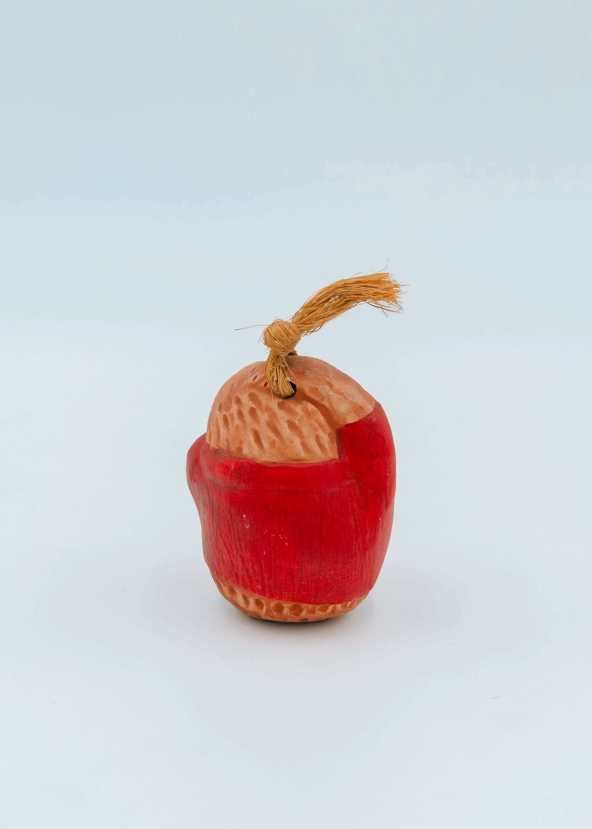 Back side of an anonymous Showa-era monkey pottery bell, showcasing the deep red mineral pigment and rustic, dimpled earth texture of the Nogomi craft.