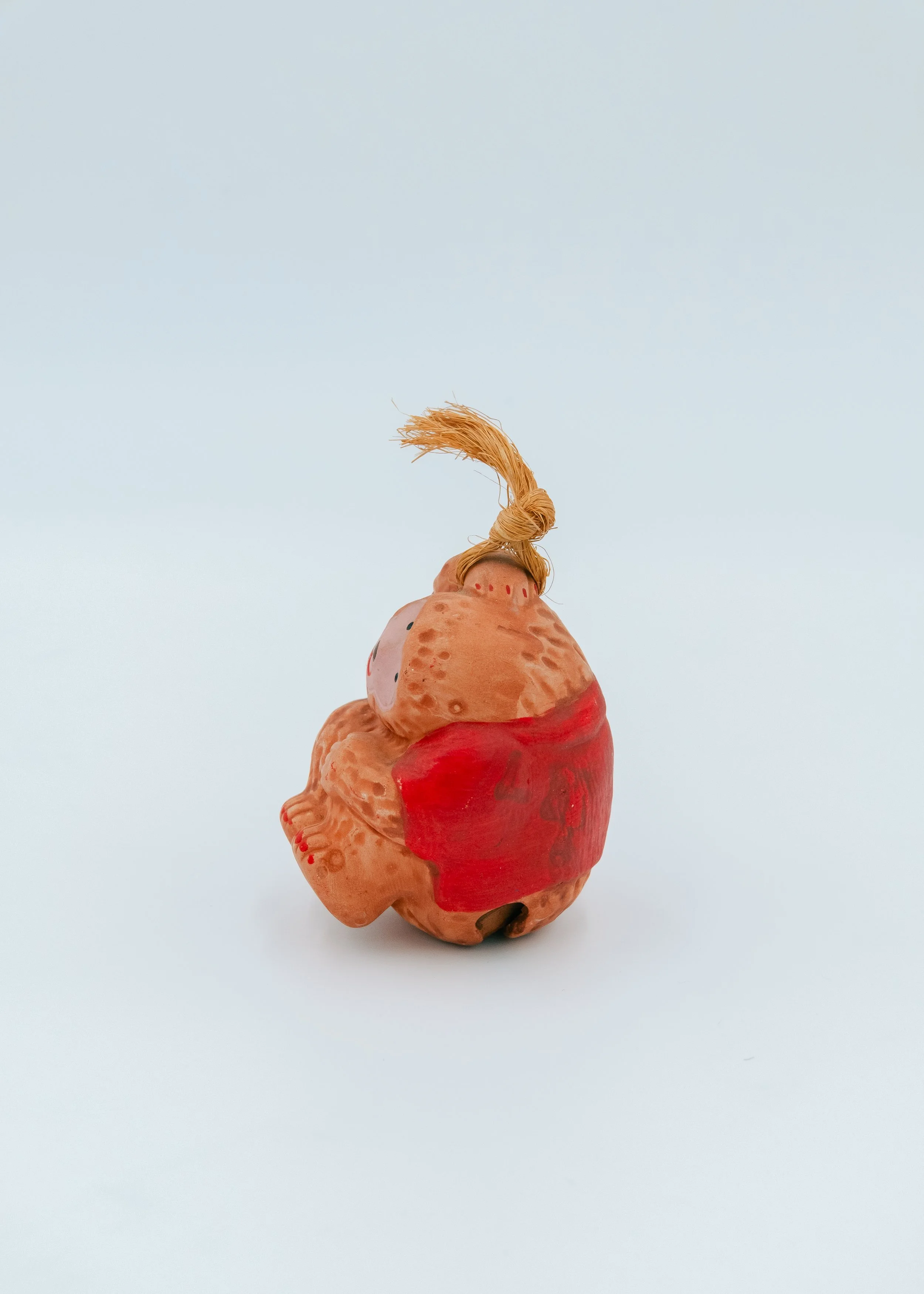 Side profile of a seated Japanese macaque clay spirit huddle posture, representing the humble bravery of post-war Mingei folk art.