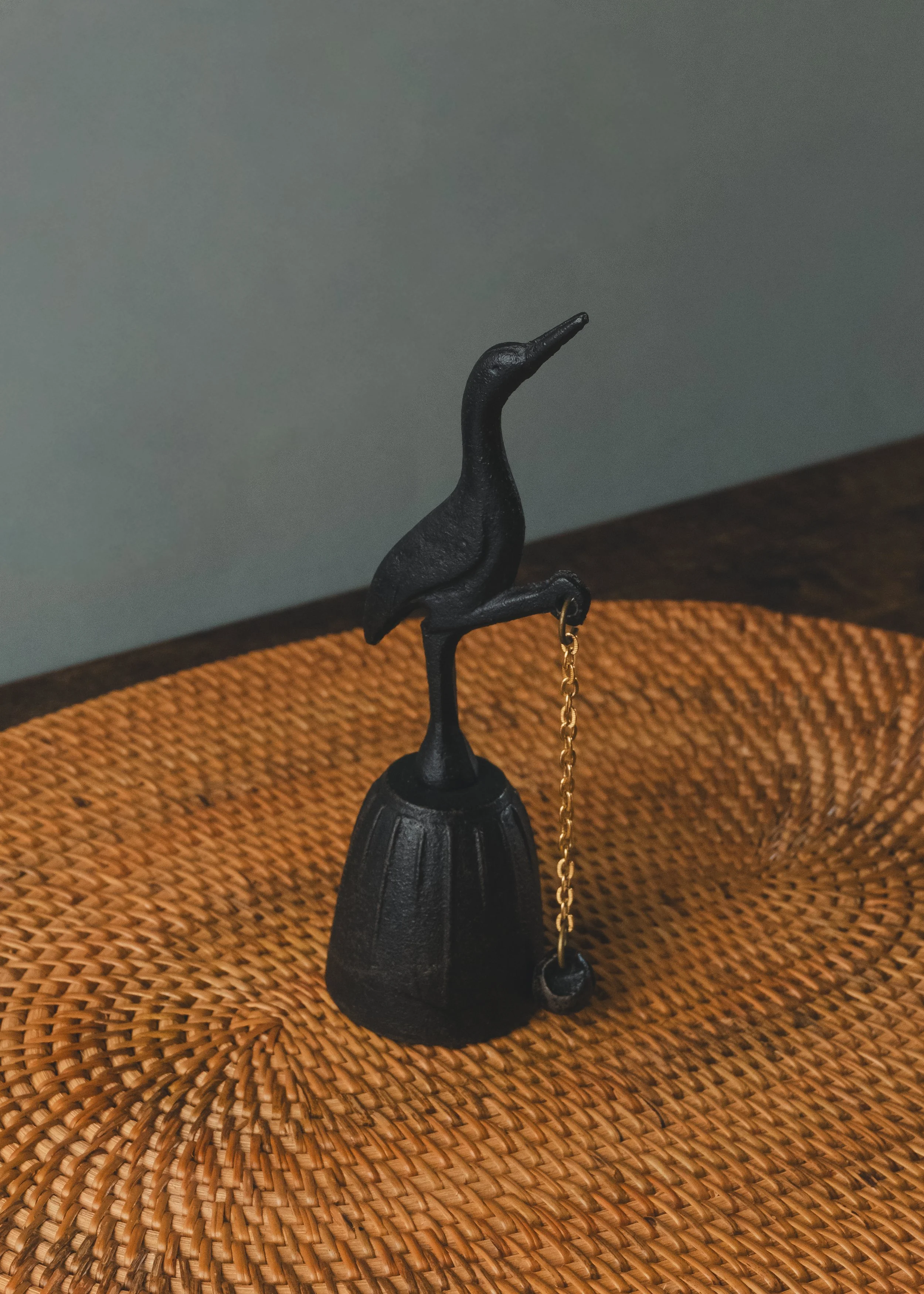Nambu Tekki iron crane table bell silhouette on a woven surface. Traditional Japanese cast iron bell from the 1970s, designed for spatial purification and minimalist decor.