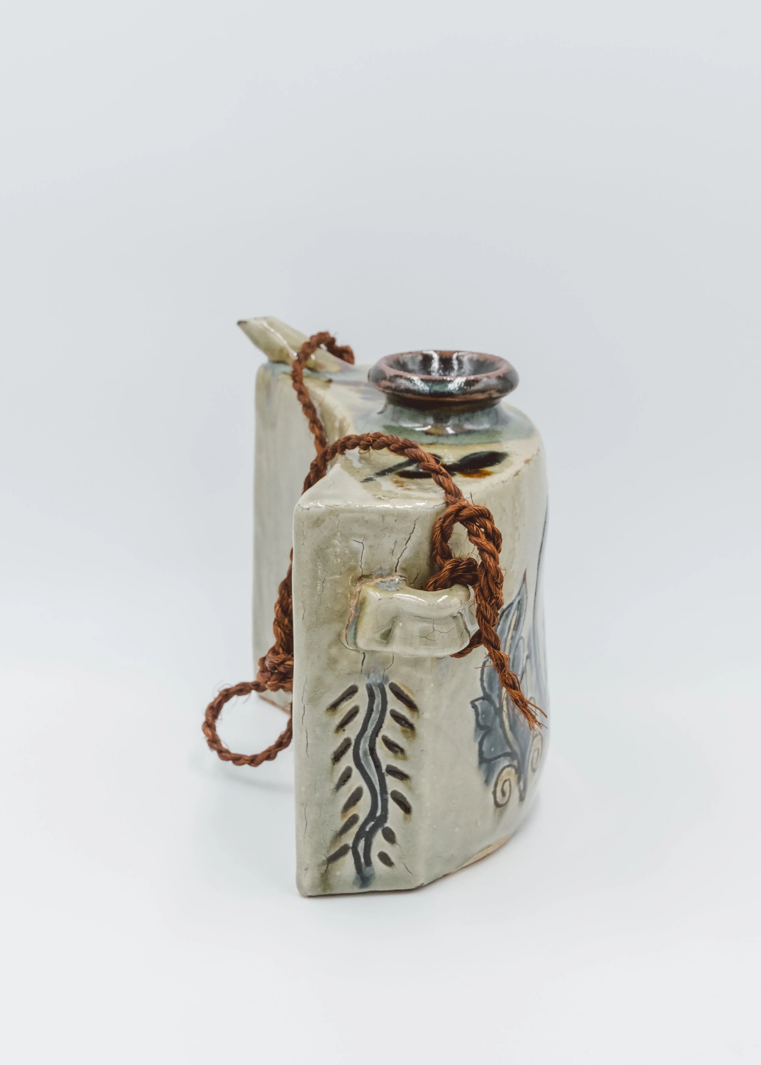 Three-quarter view of a vintage Okinawan Dachibin ceramic bell with fish patterns and a brown ritual cord.