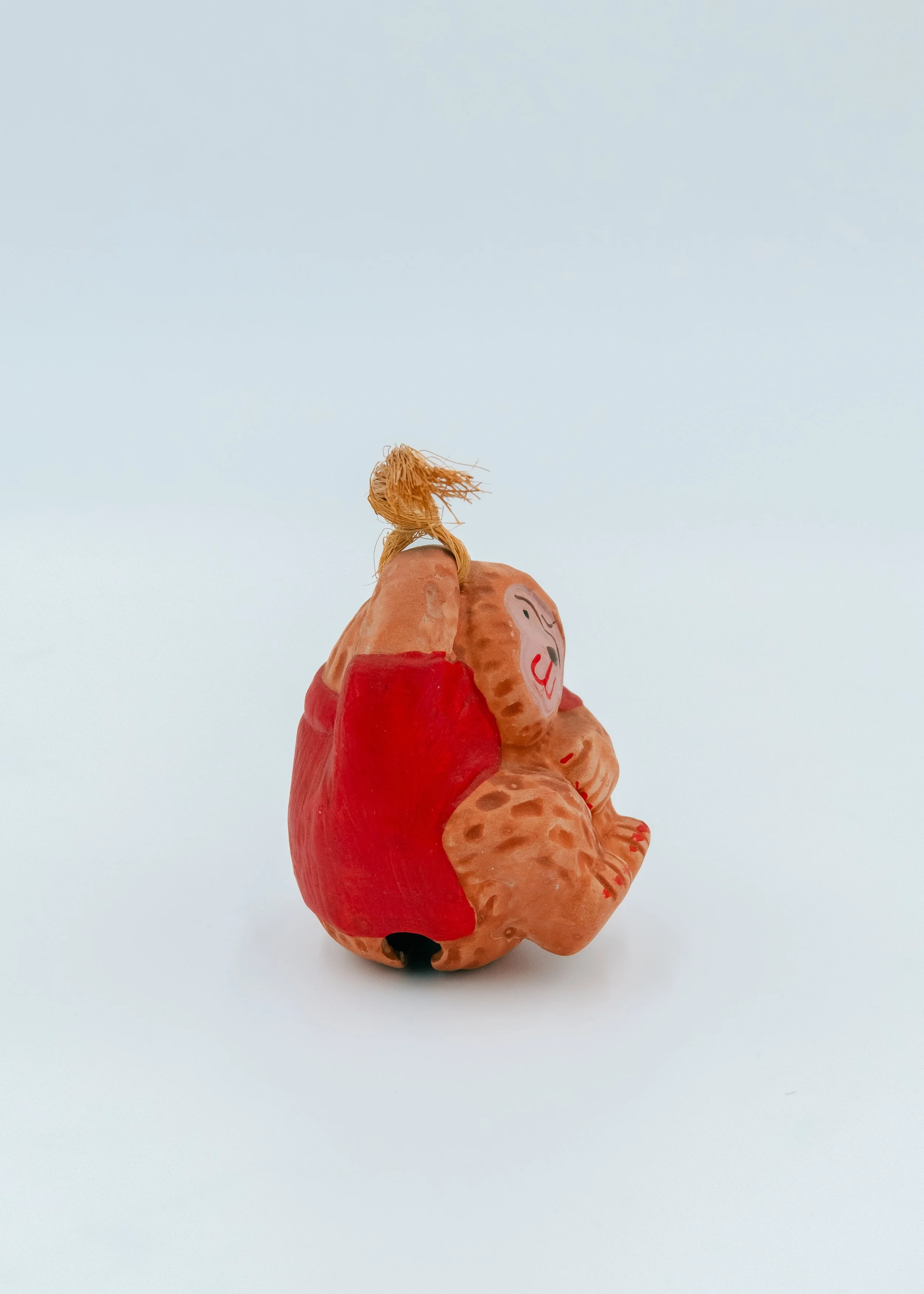 Side profile of a seated Japanese macaque clay spirit huddle posture, representing the humble bravery of post-war Mingei folk art.