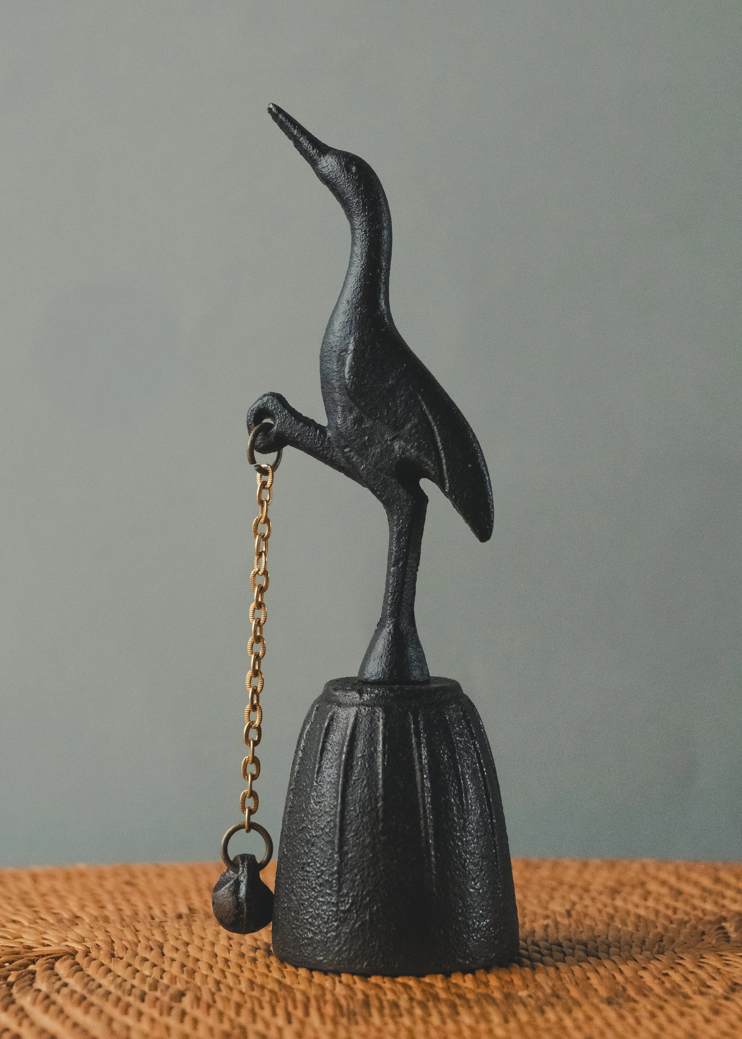 Side profile of the ARCHETYPE: CRANE BELL 1970. An anonymous Japanese iron masterpiece of a standing crane, serving as a functional sonic monument for meditation.