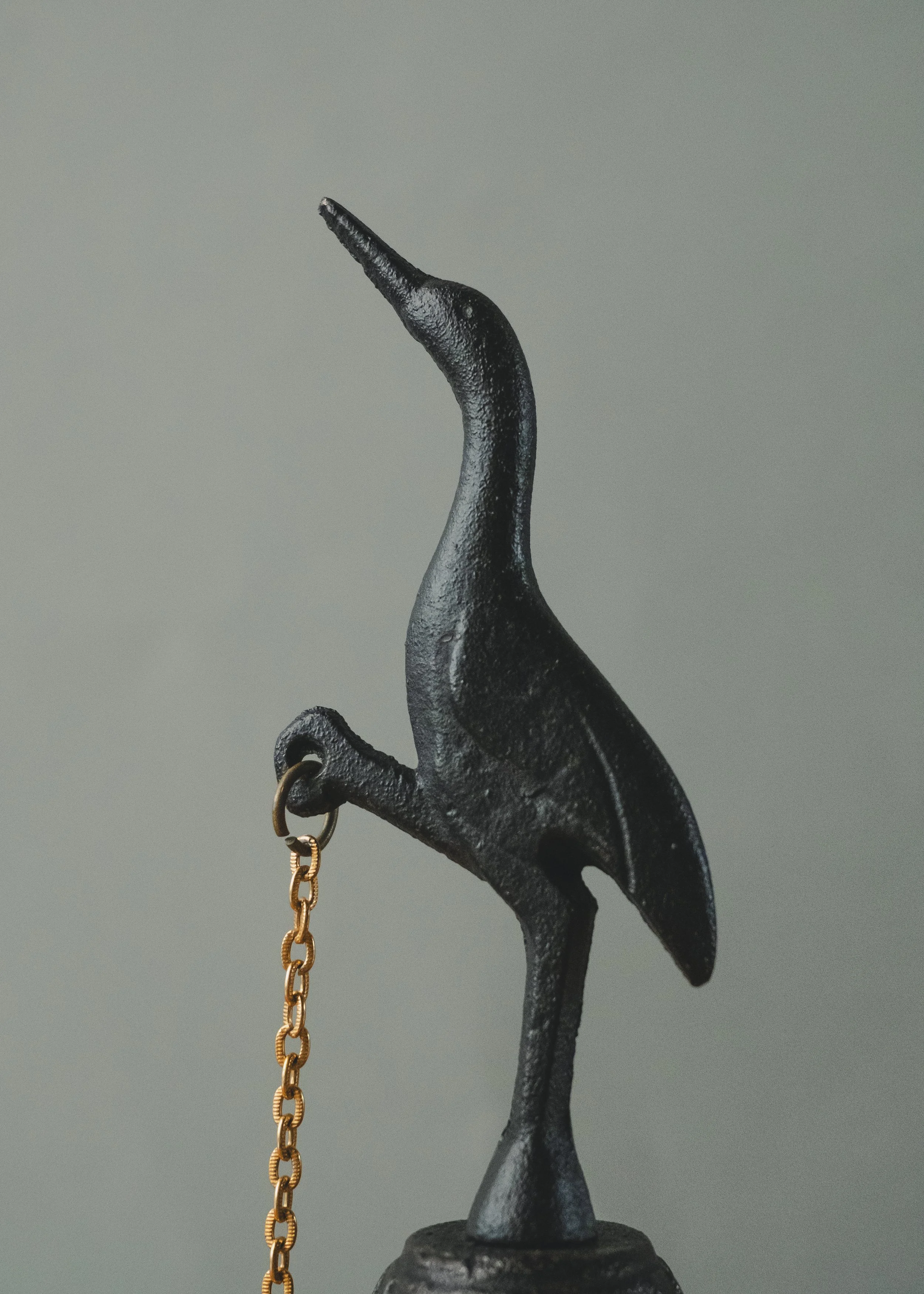 Side profile of the ARCHETYPE: CRANE BELL 1970. An anonymous Japanese iron masterpiece of a standing crane, serving as a functional sonic monument for meditation.