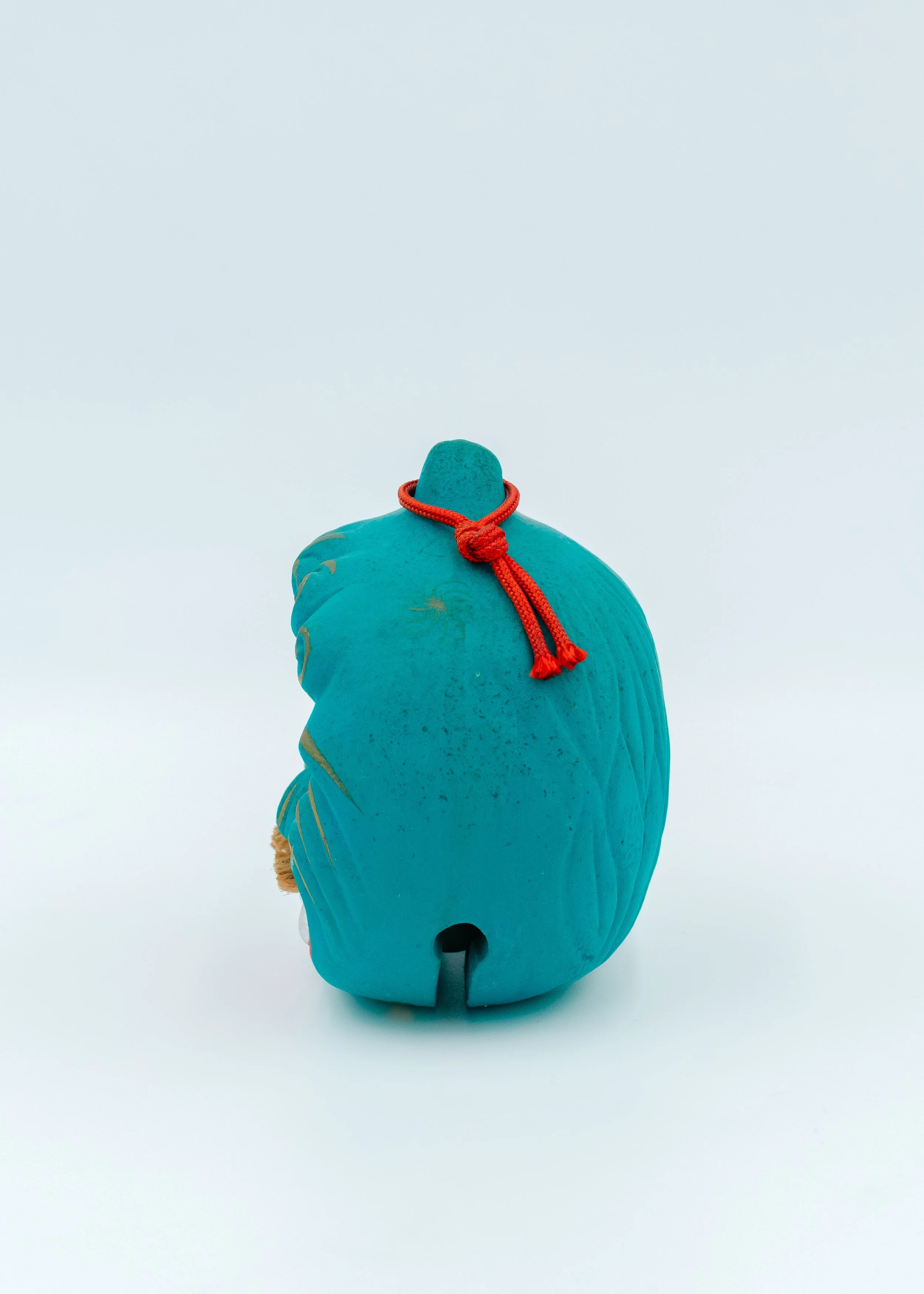 Reverse side view of a vintage Japanese turquoise clay amulet showing the textured hand-formed curves and a traditional red cord, authentic Nogomi spirit.