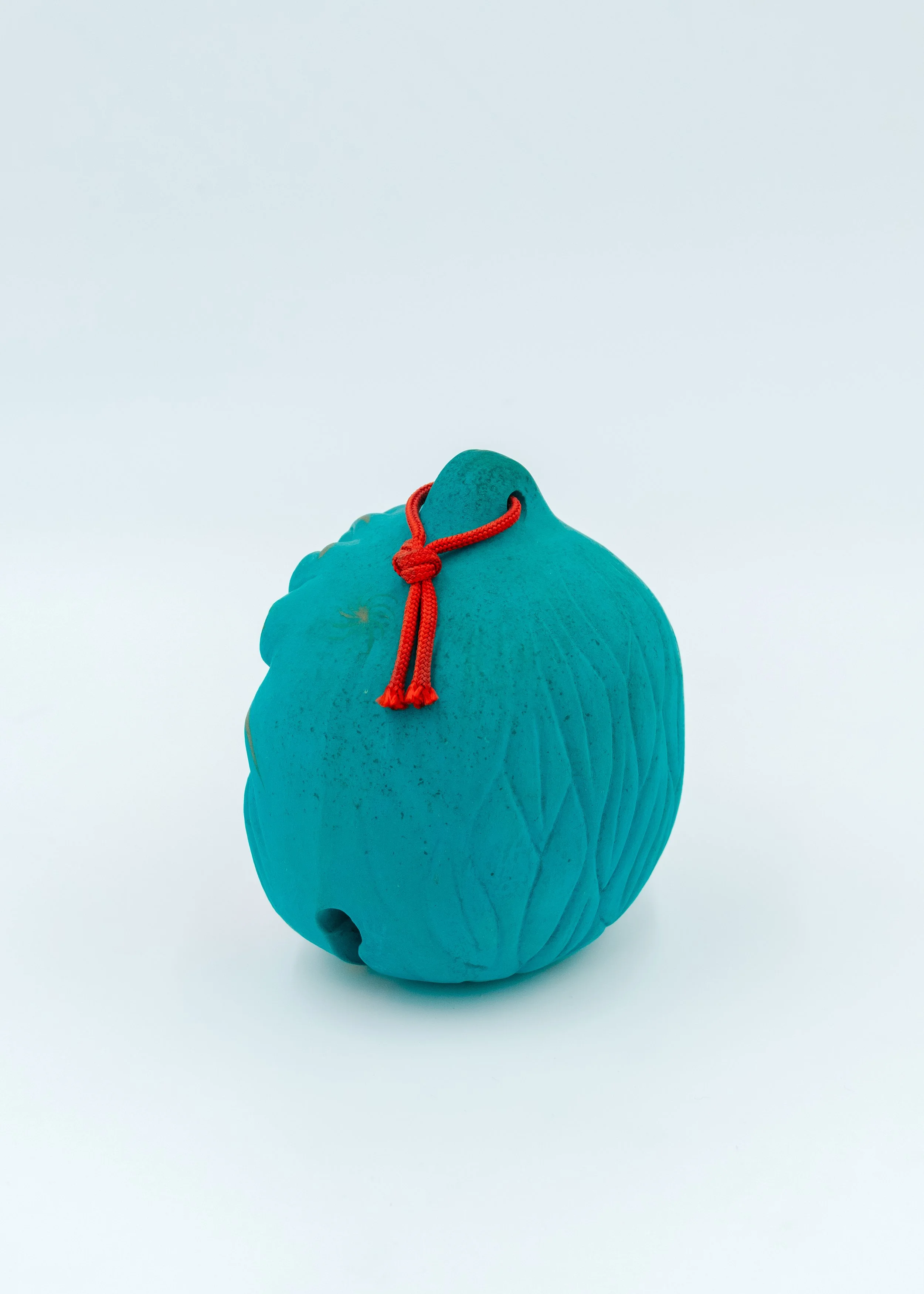 Reverse side view of a vintage Japanese turquoise clay amulet showing the textured hand-formed curves and a traditional red cord, authentic Nogomi spirit.