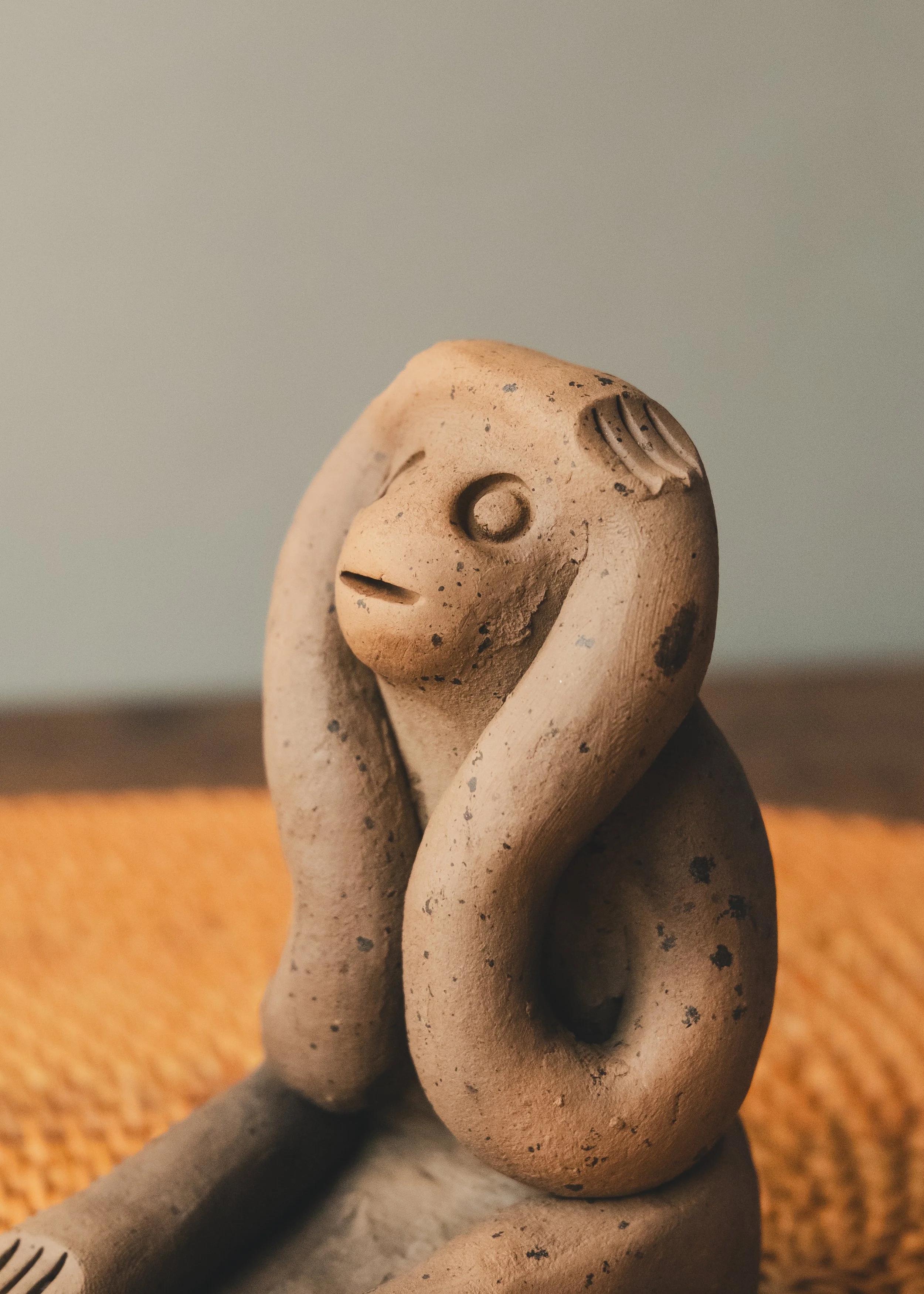 Side angle of a hand-molded "Hear No Evil" earthenware simian sculpture. Unglazed red clay retaining the smoke-stained patina from a 1,300-year-old traditional Japanese kiln process.