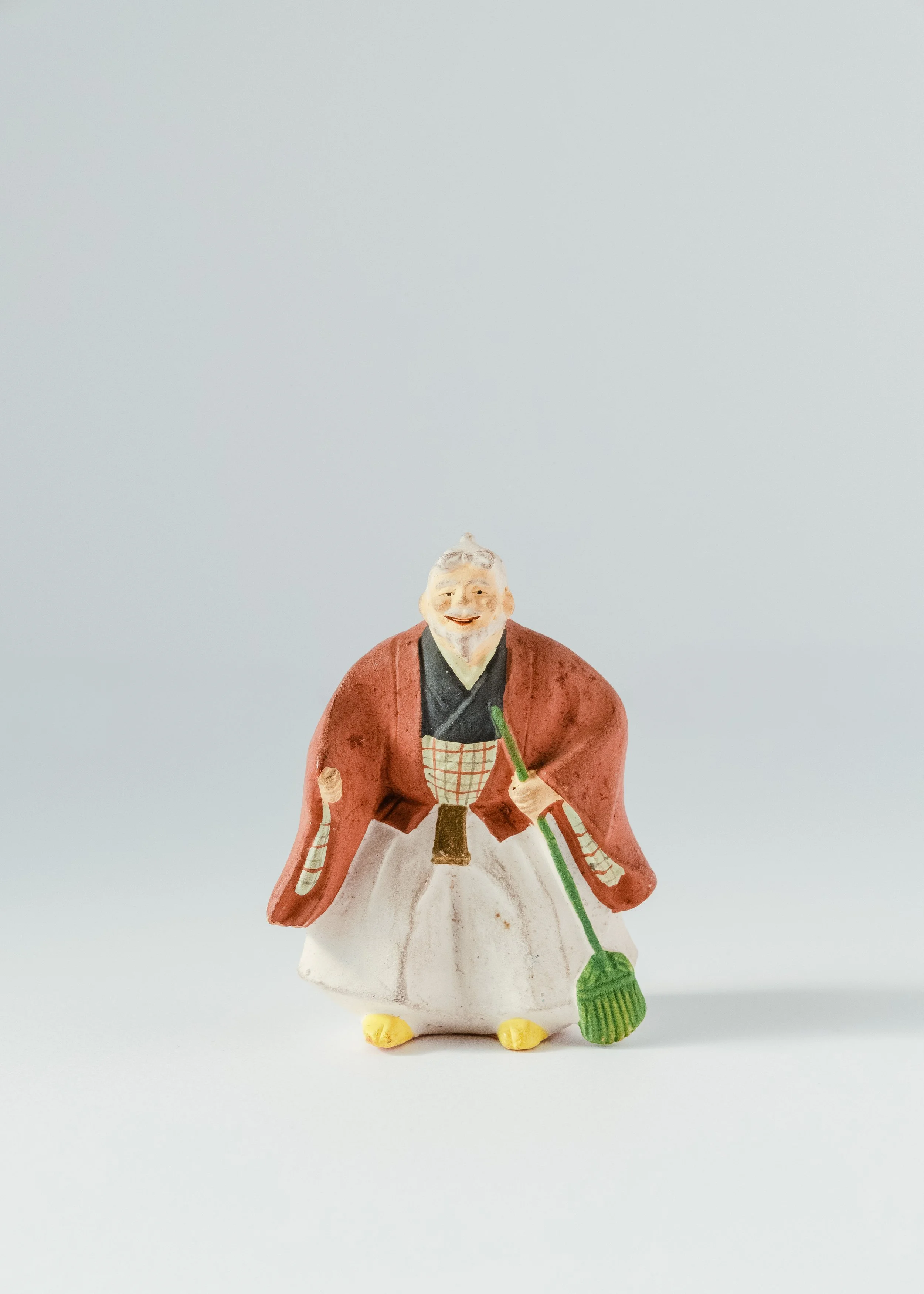 Front view of smiling old man clay doll holding broom Takasago legend symbol of happy marriage