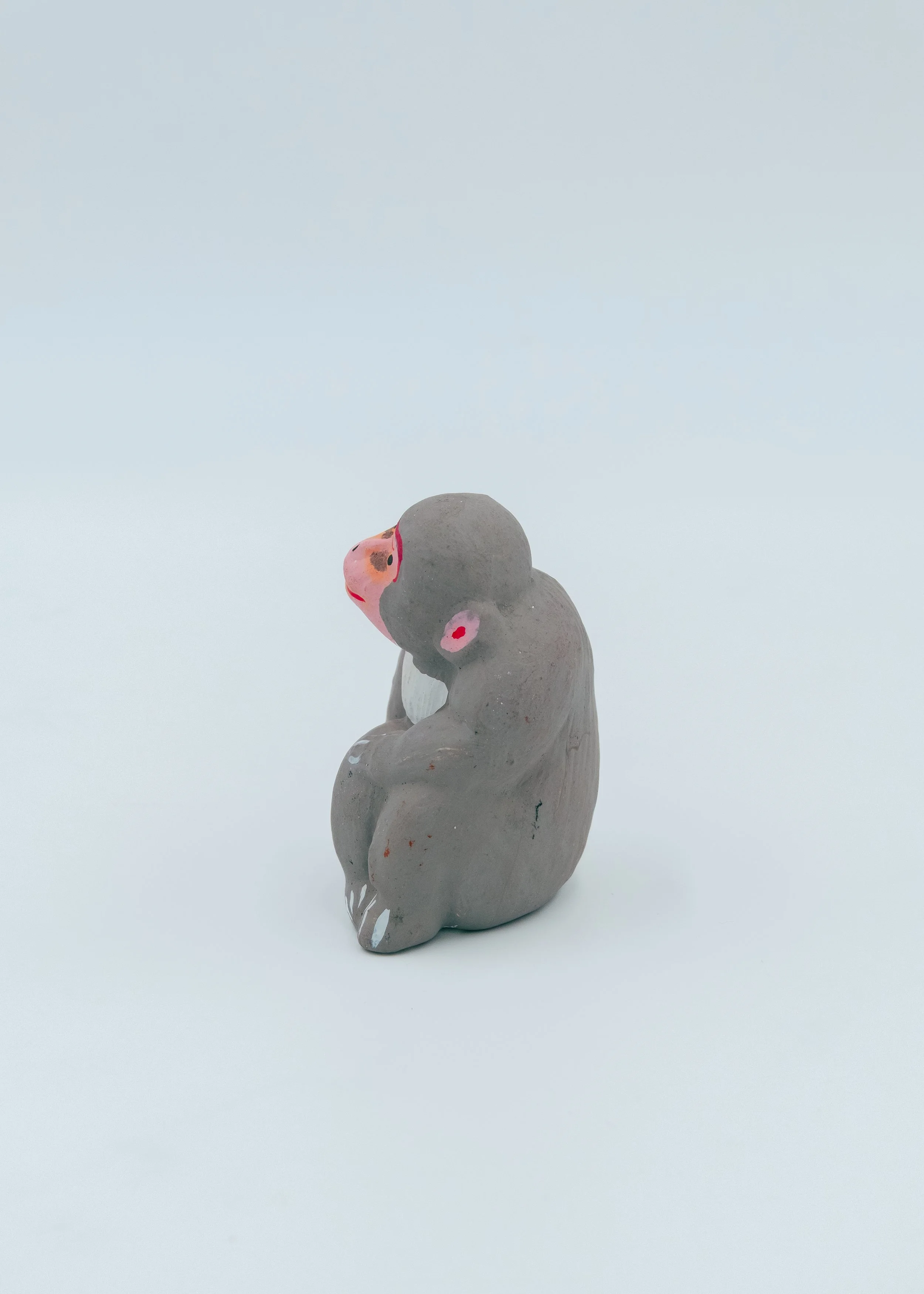 Reverse side of an anonymous Showa-era clay monkey ornament, showcasing the rustic matte grey earthen texture and artisan-formed curves.