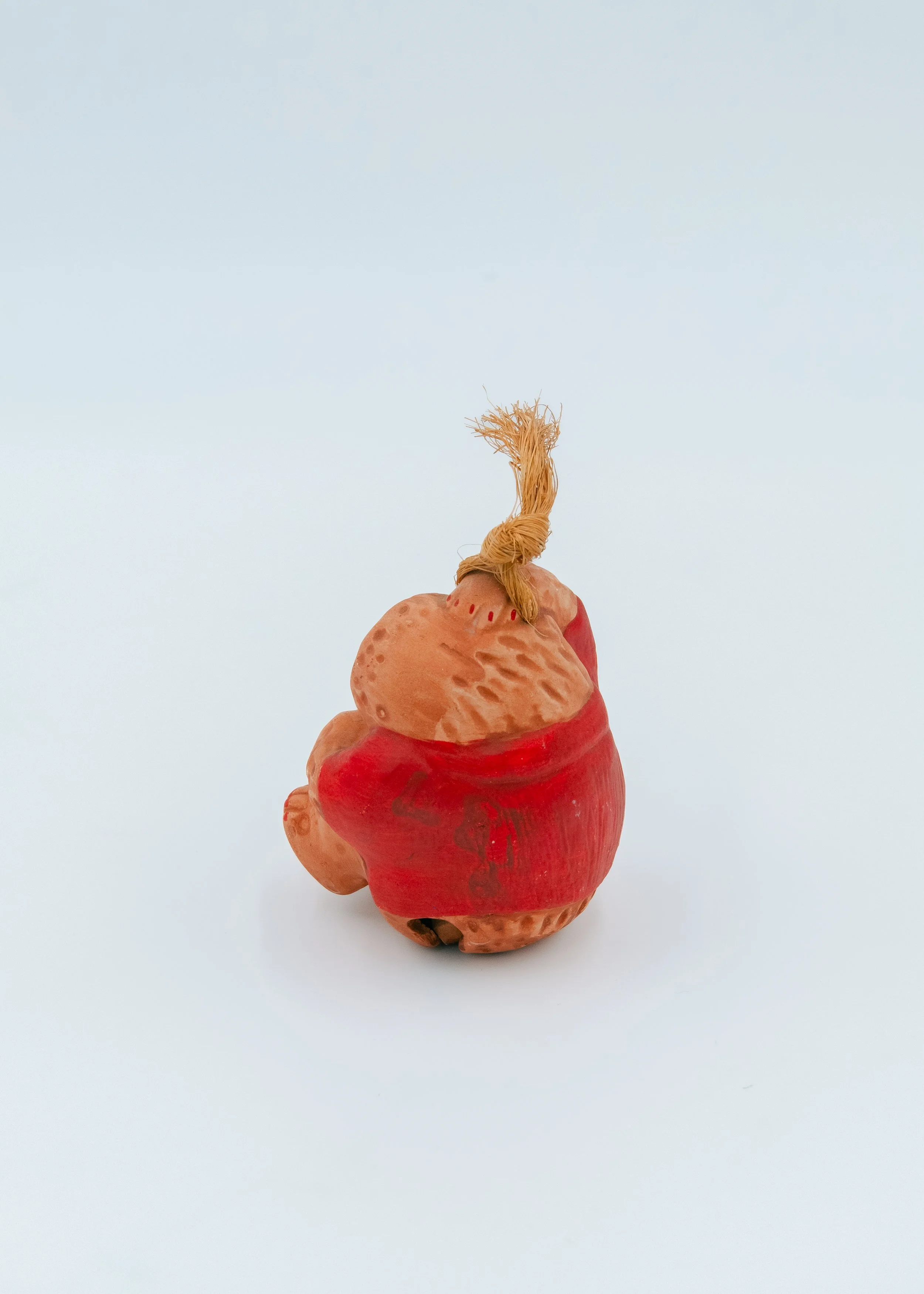 Back side of an anonymous Showa-era monkey pottery bell, showcasing the deep red mineral pigment and rustic, dimpled earth texture of the Nogomi craft.