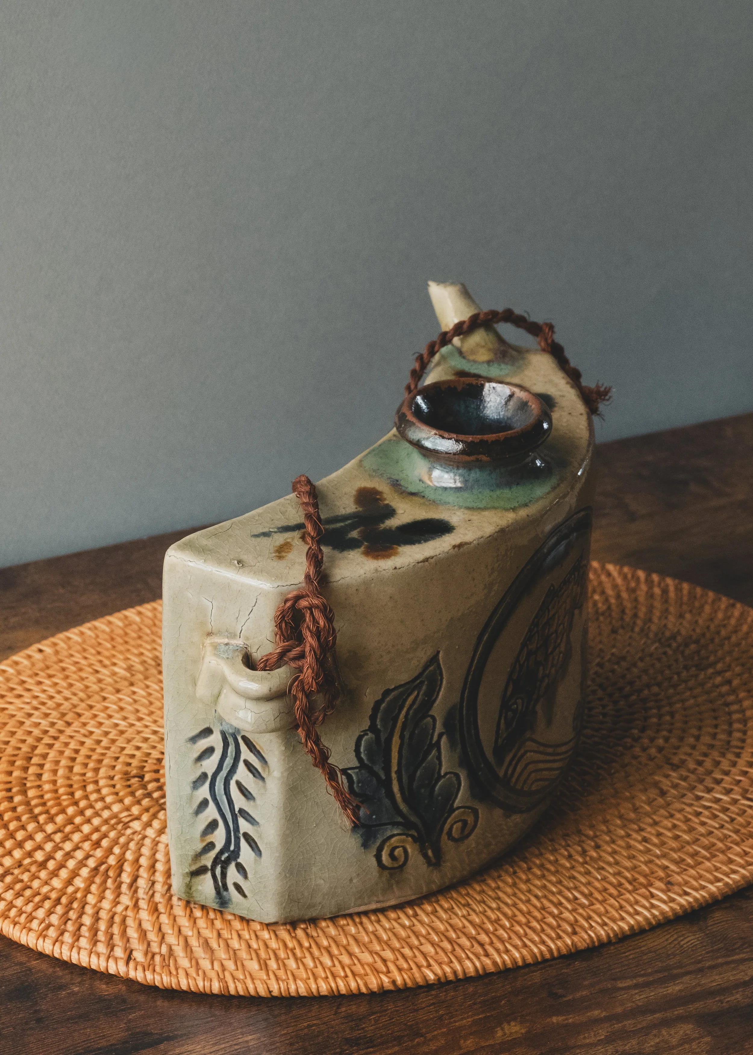Authentic Tsuboya-yaki crescent-moon shaped pottery flask sitting on a rattan mat, Japan Mingei archive.