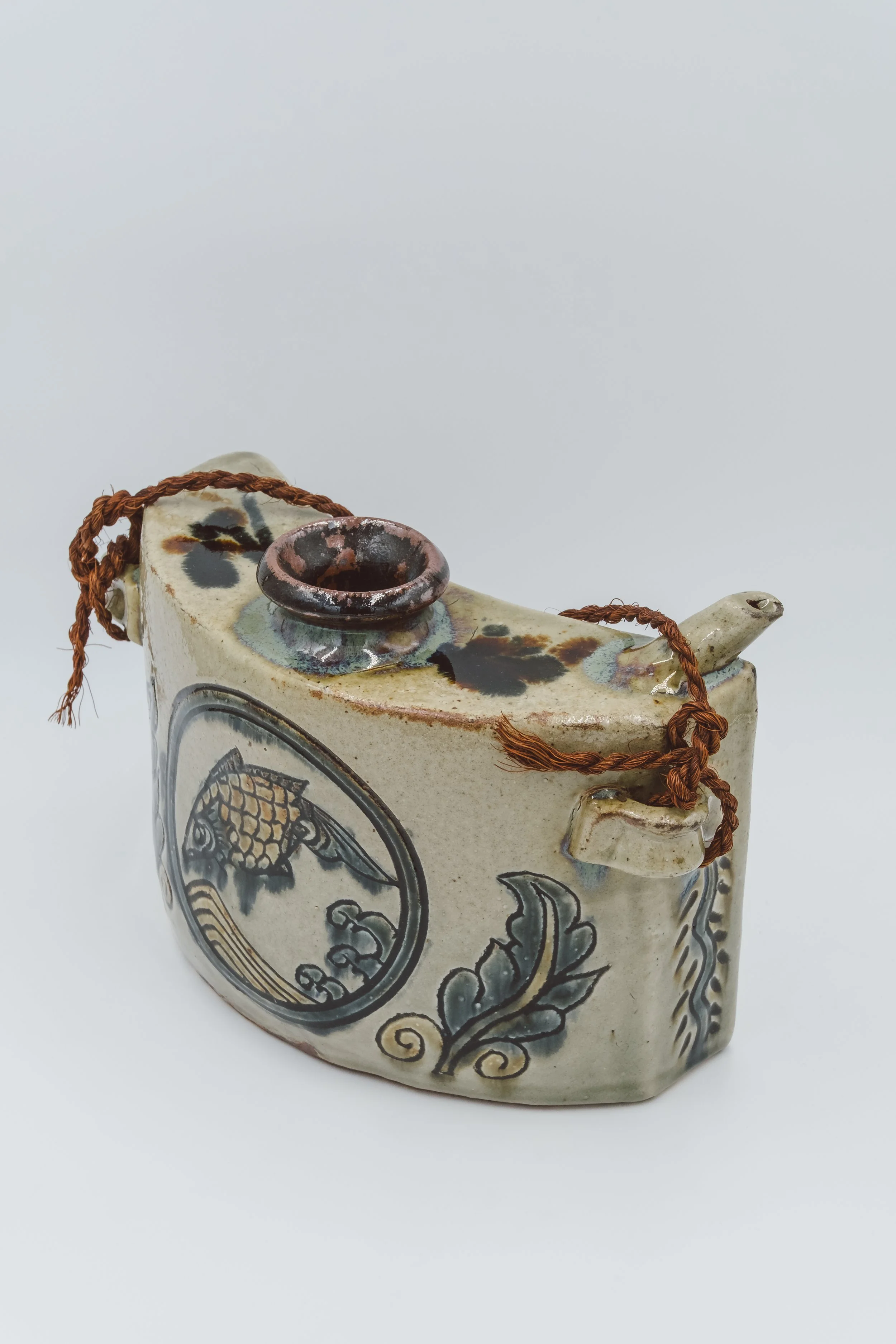 Three-quarter view of a vintage Okinawan Dachibin ceramic bell with fish patterns and a brown ritual cord.