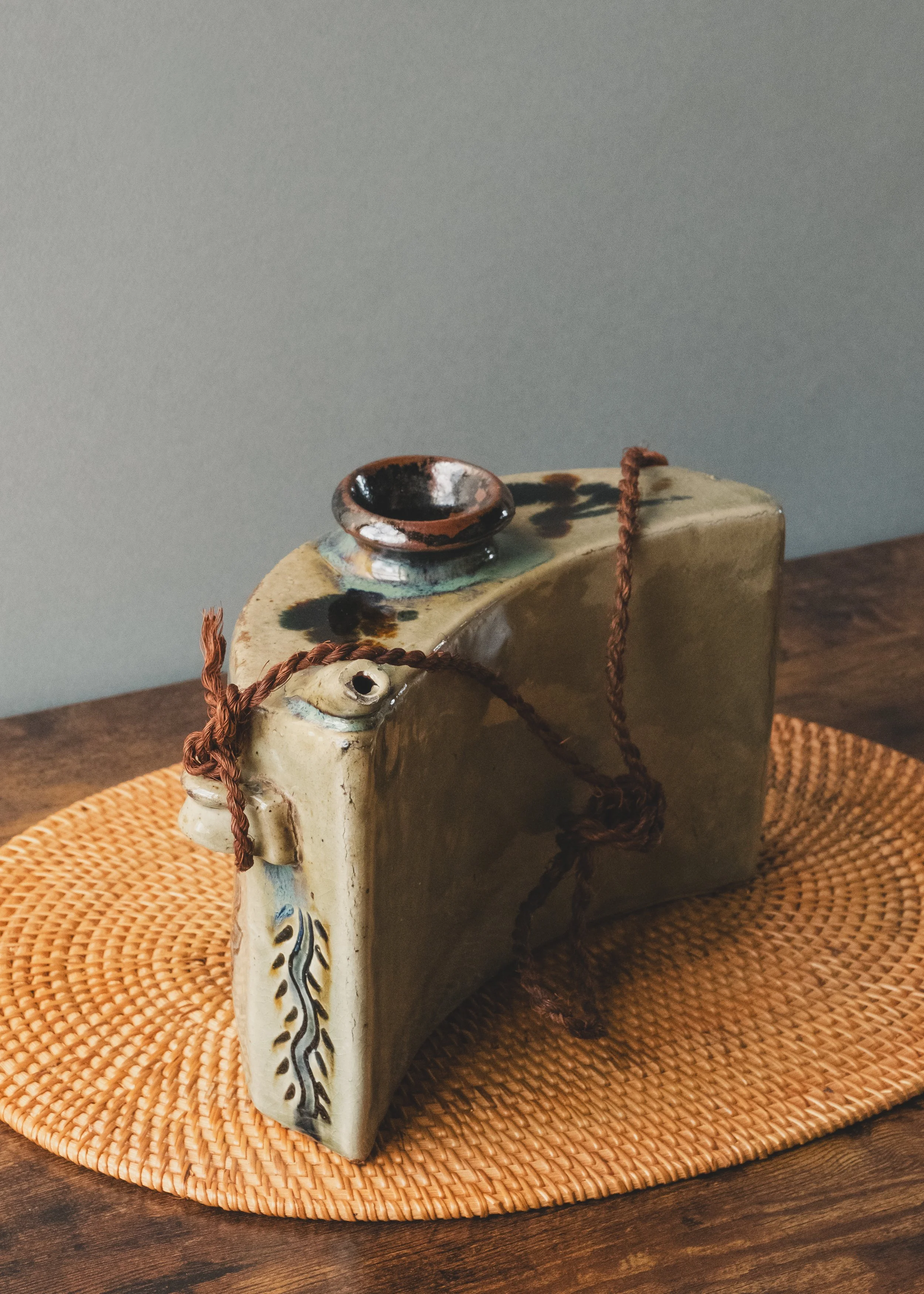 Three-quarter view of a vintage Okinawan Dachibin ceramic bell with fish patterns and a brown ritual cord.