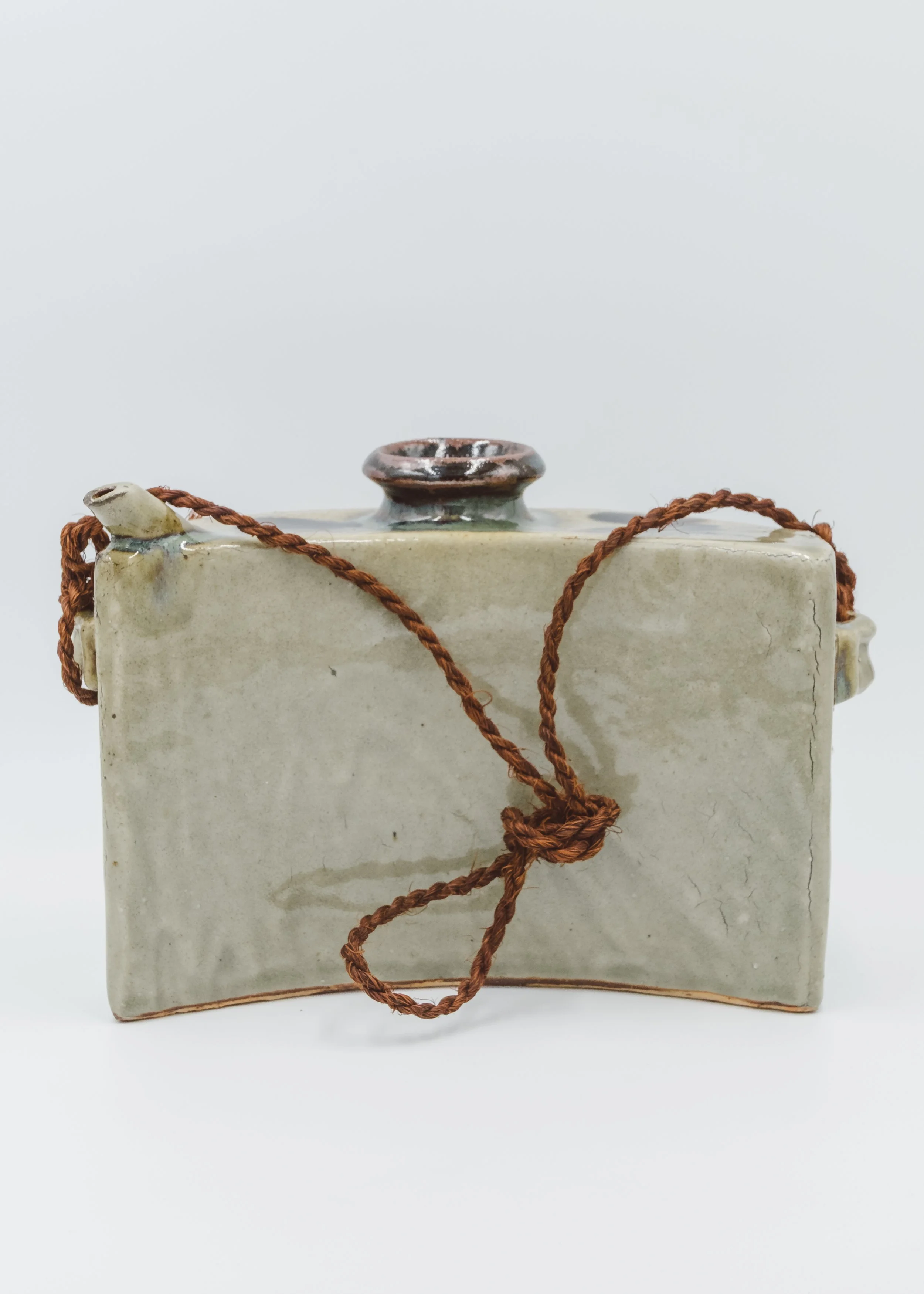 Profile view of a Japanese handmade clay bell (Tsuchi-rei) showing the ergonomic curved structure for portable use.