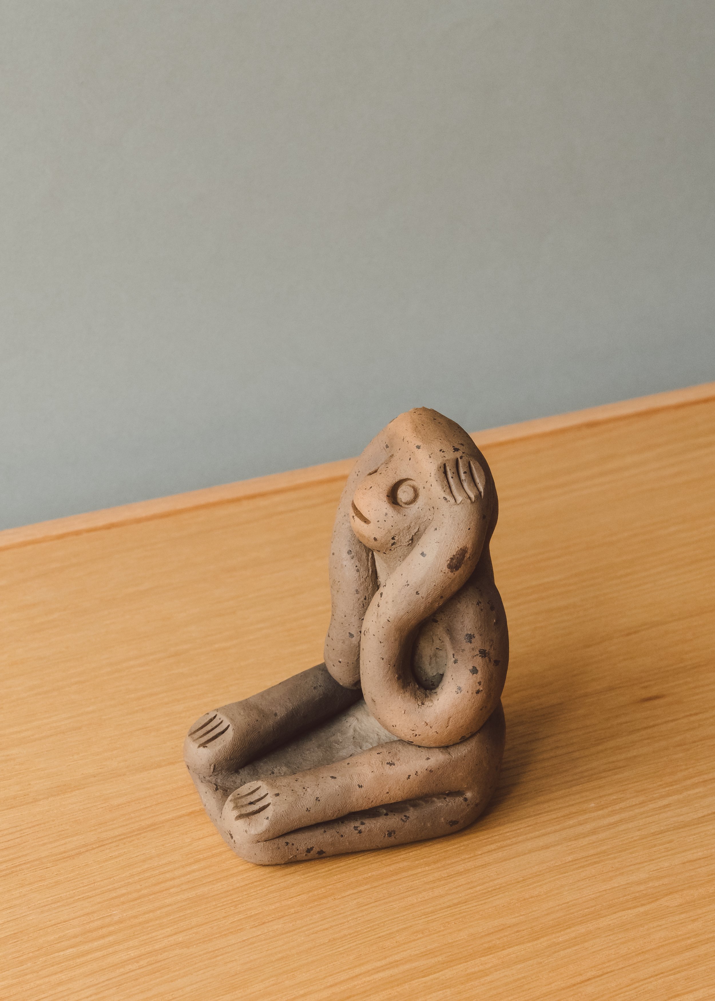 Side angle of a hand-molded "Hear No Evil" earthenware simian sculpture. Unglazed red clay retaining the smoke-stained patina from a 1,300-year-old traditional Japanese kiln process.