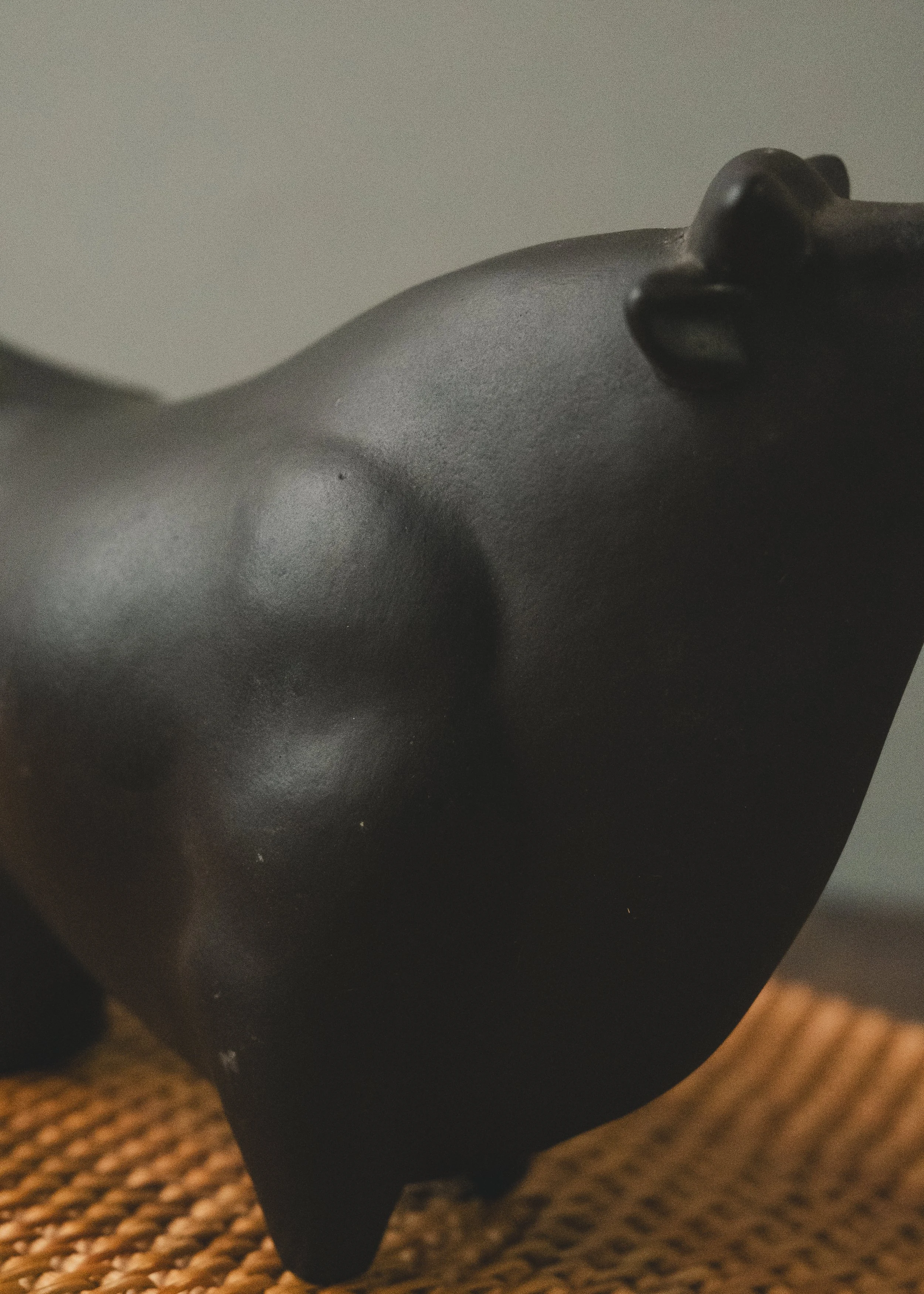 View of the smooth, arched back of a Japanese matte-black bull sculpture. Highlighting the essentialist geometry and the refined, timeless aesthetic of Japanese Mingei pottery.