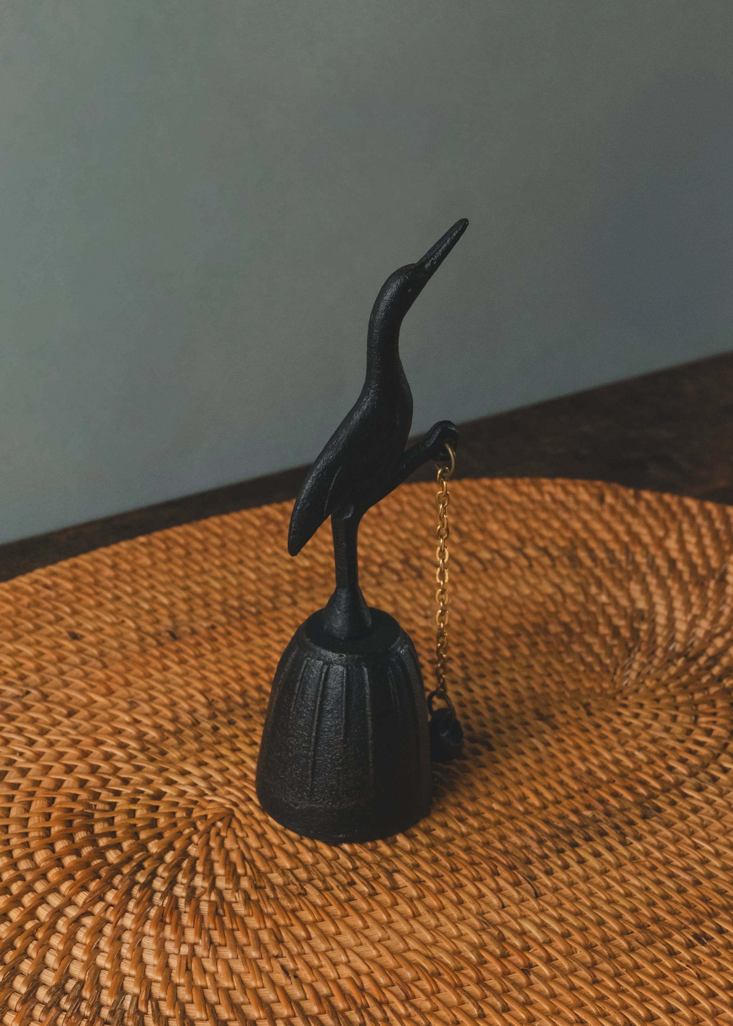 Nambu Tekki iron crane table bell silhouette on a woven surface. Traditional Japanese cast iron bell from the 1970s, designed for spatial purification and minimalist decor.