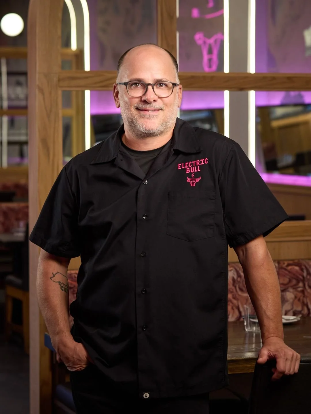 Chef Justin Severino wearing a shirt with 'Electric Bull' embroidered on it, standing inside Electric Bull