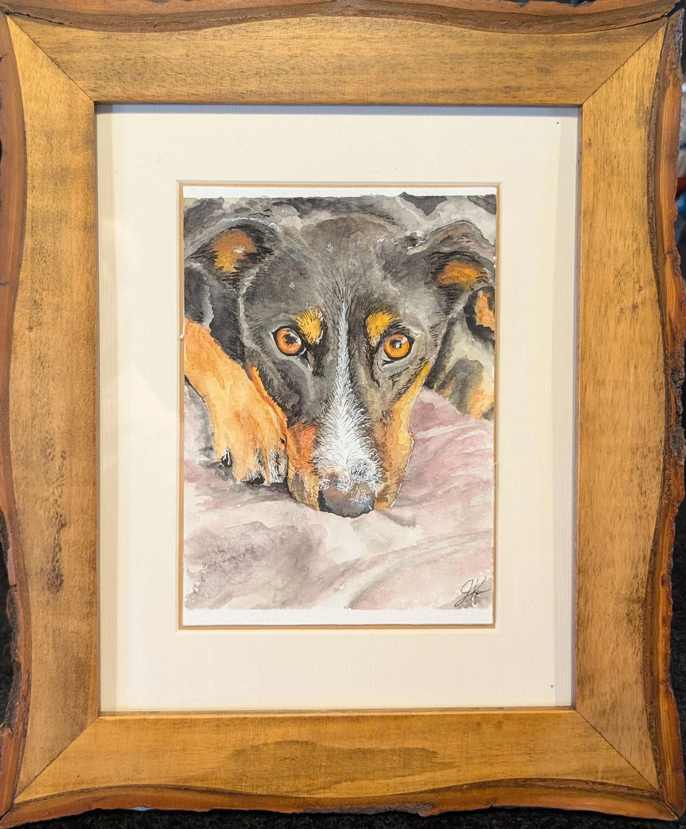 Watercolor painting of a wolf's face with piercing yellow eyes and detailed fur, framed in a wooden frame.