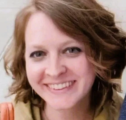 Close-up of a smiling woman with shoulder-length wavy red hair.
