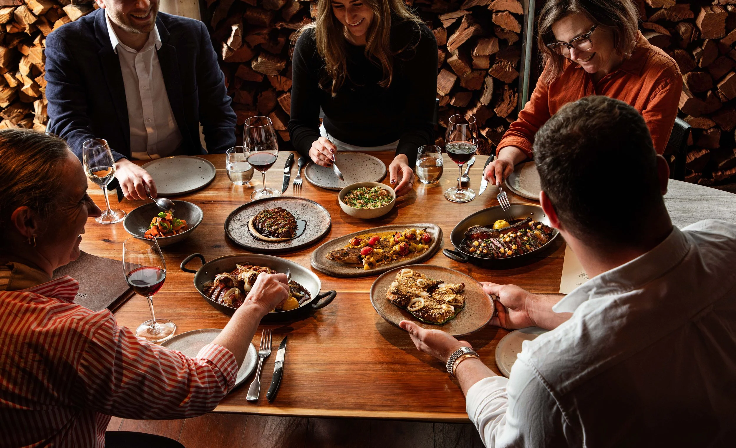 People enjoying a dinner gathering around a wooden table with various dishes and glasses of wine.