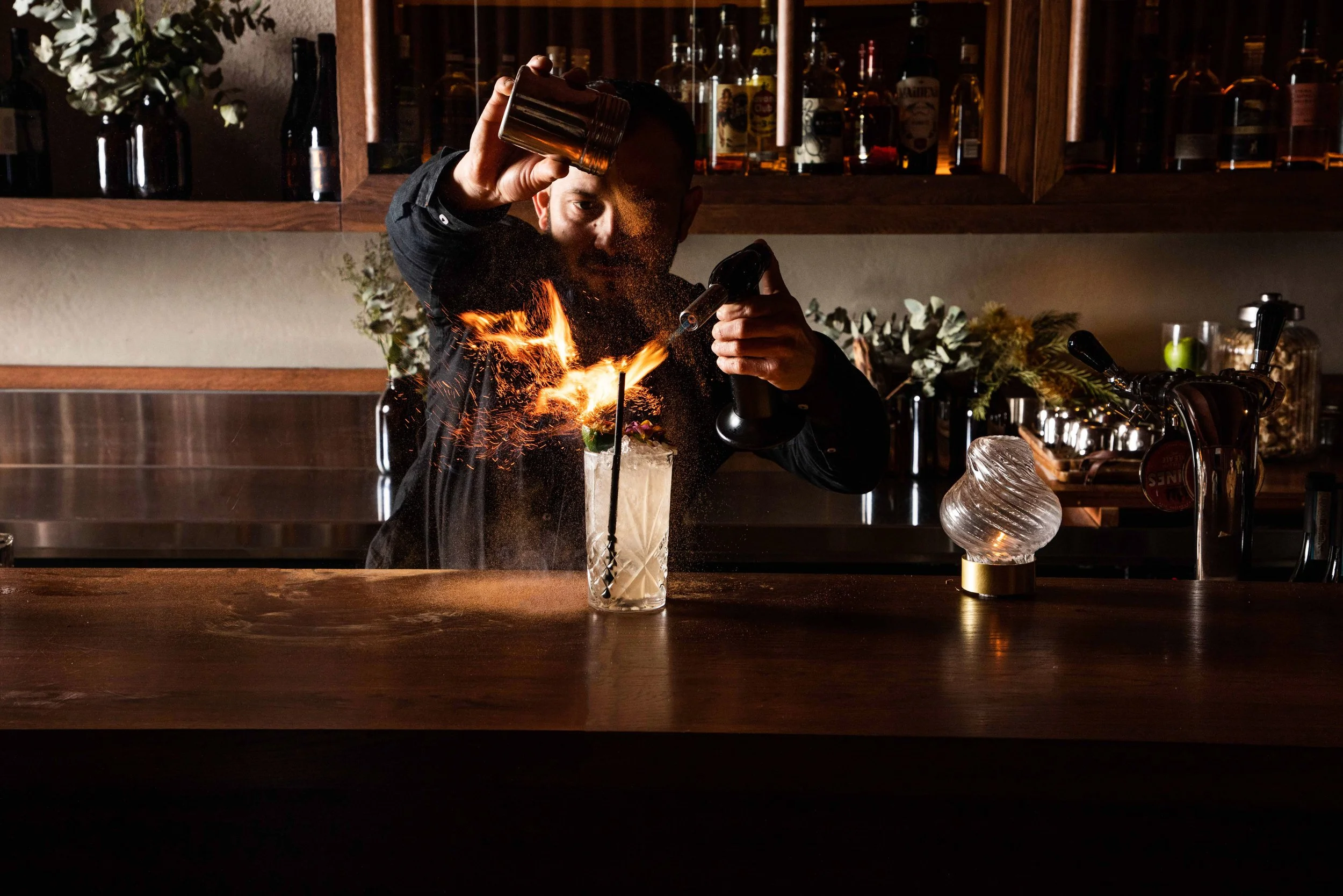 Bartender making a cocktail with a flame, in a dimly lit bar.