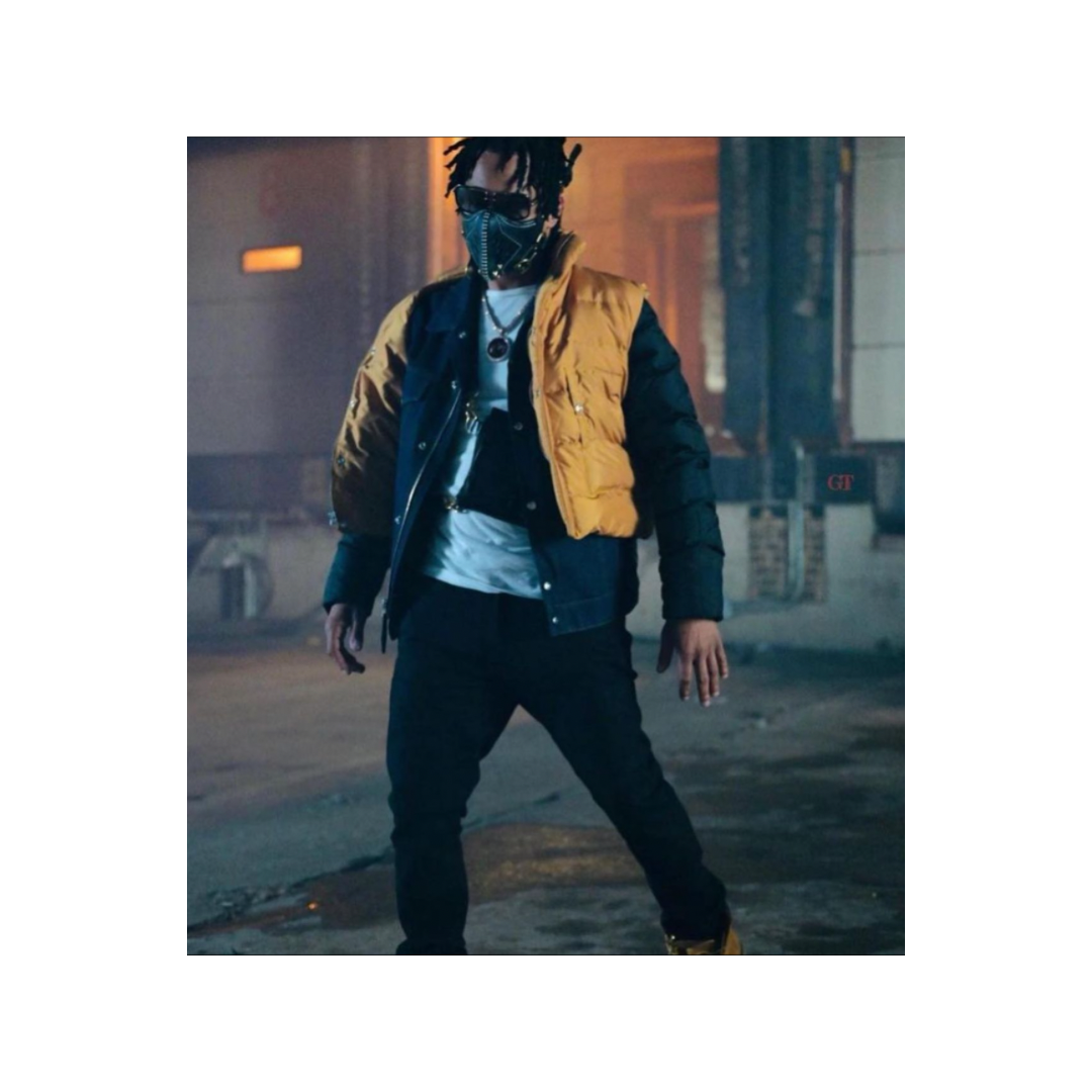 A person wearing a yellow and black jacket, black pants, yellow boots, sunglasses, and a face mask, standing outdoors at night in an urban setting with buildings and streetlights in the background.