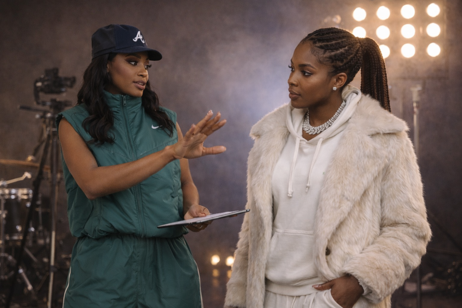 Two women having a conversation in a film or TV set, with professional lighting and cameras in the background.