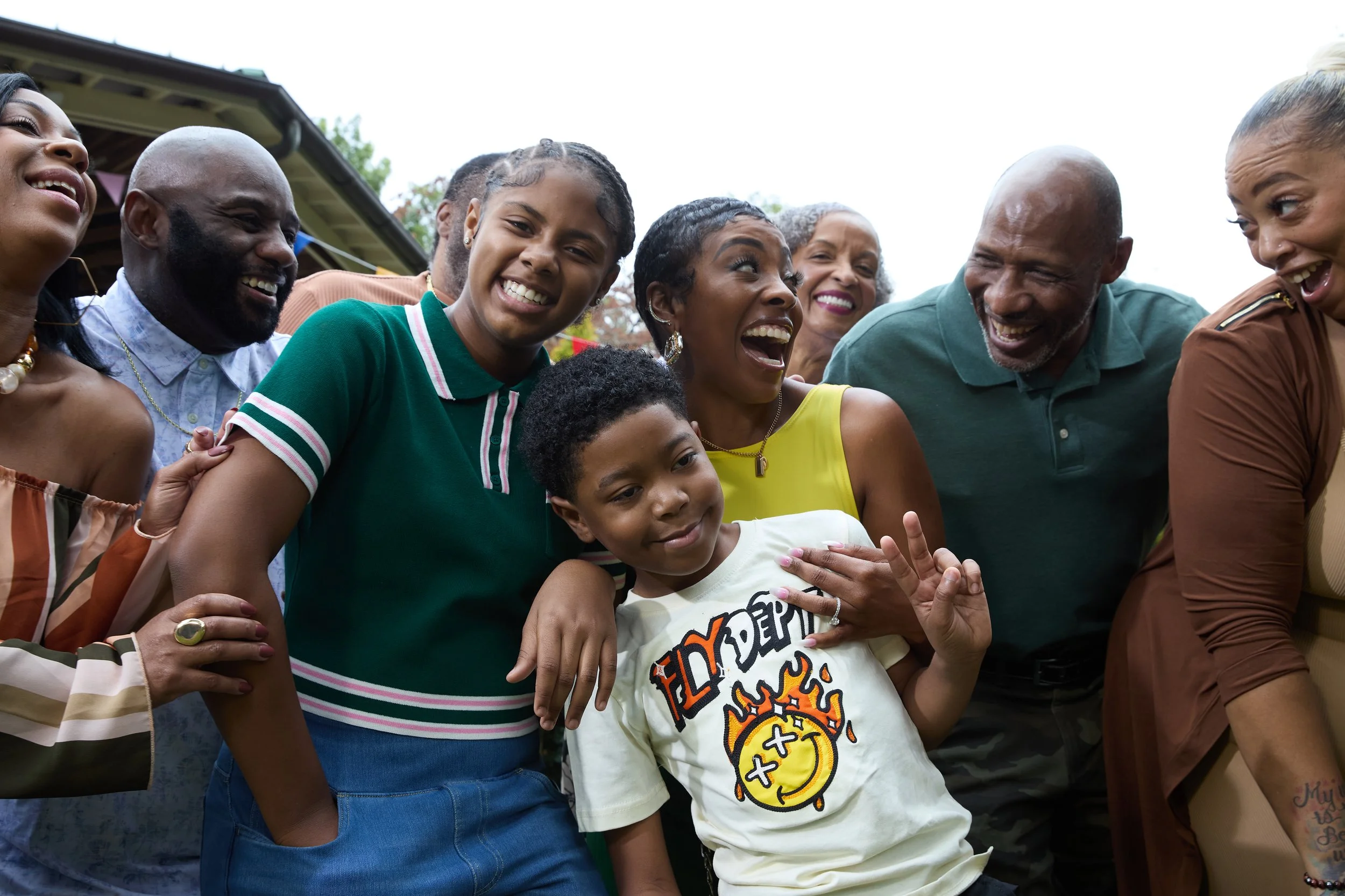 Group of diverse people smiling, laughing, and hugging at an outdoor gathering.