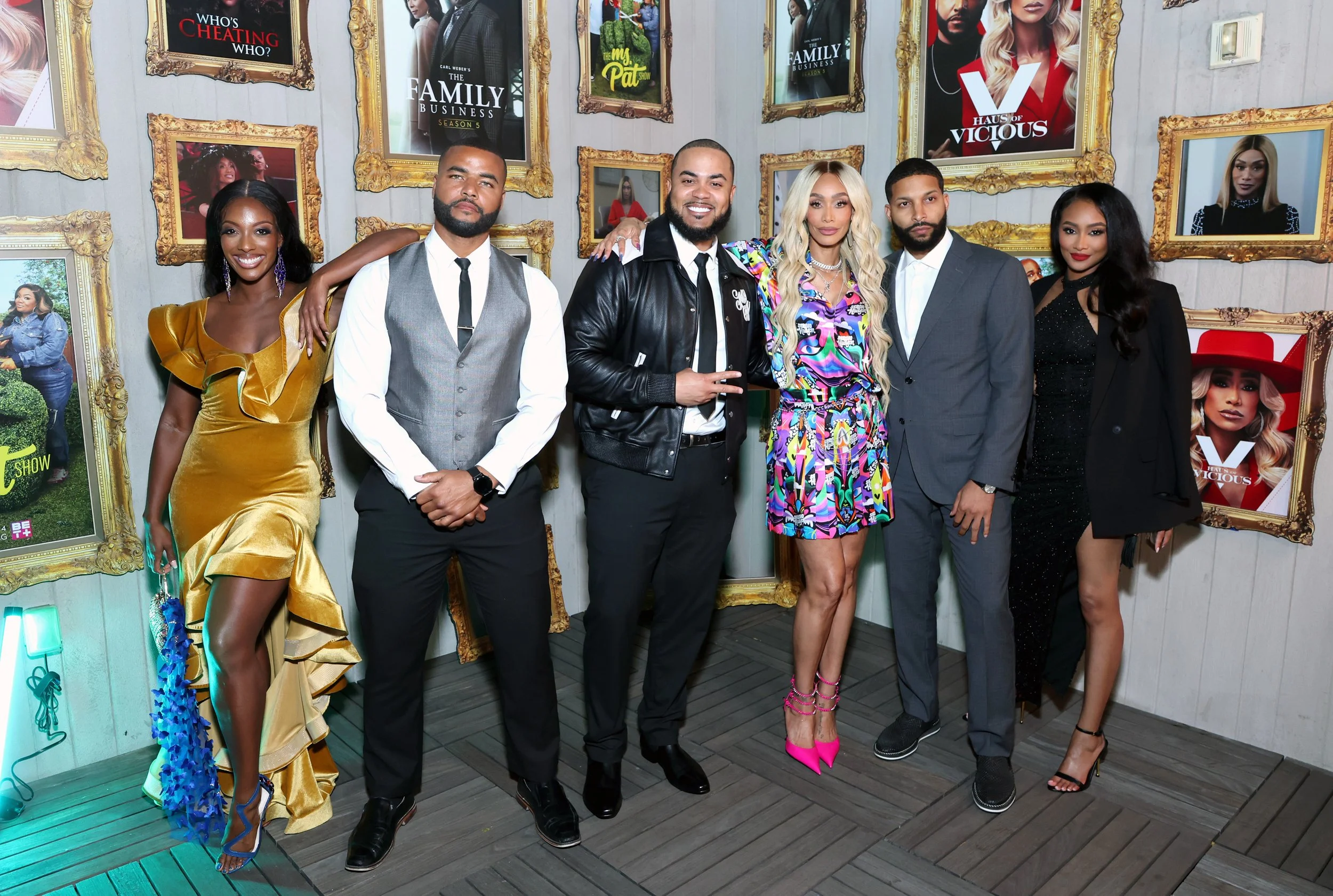 Group of seven people standing together at a promotional event with framed posters of TV shows behind them.