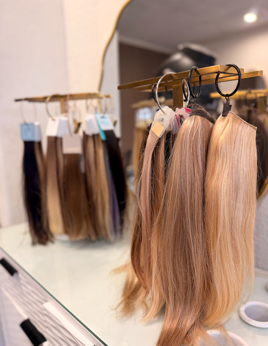 Long blonde hair extensions hanging on a rack inside a Tranquility salon.