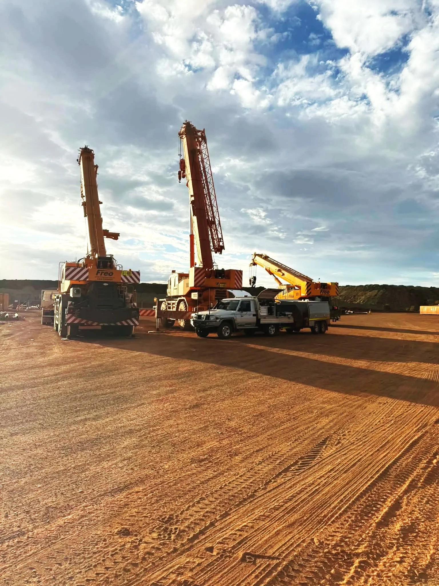 Construction site with three cranes and a pickup truck under a partly cloudy sky