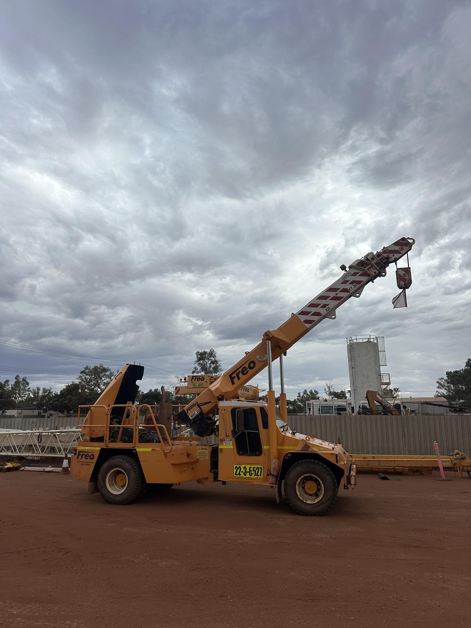 Construction forklift truck on a dirt lot with cloudy sky and construction equipment in background.