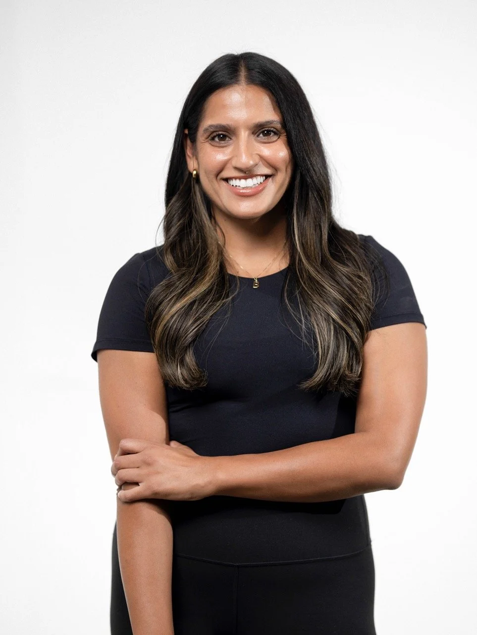 Portrait of a woman with long wavy hair, wearing a black top, smiling with arms crossed, against a white background.