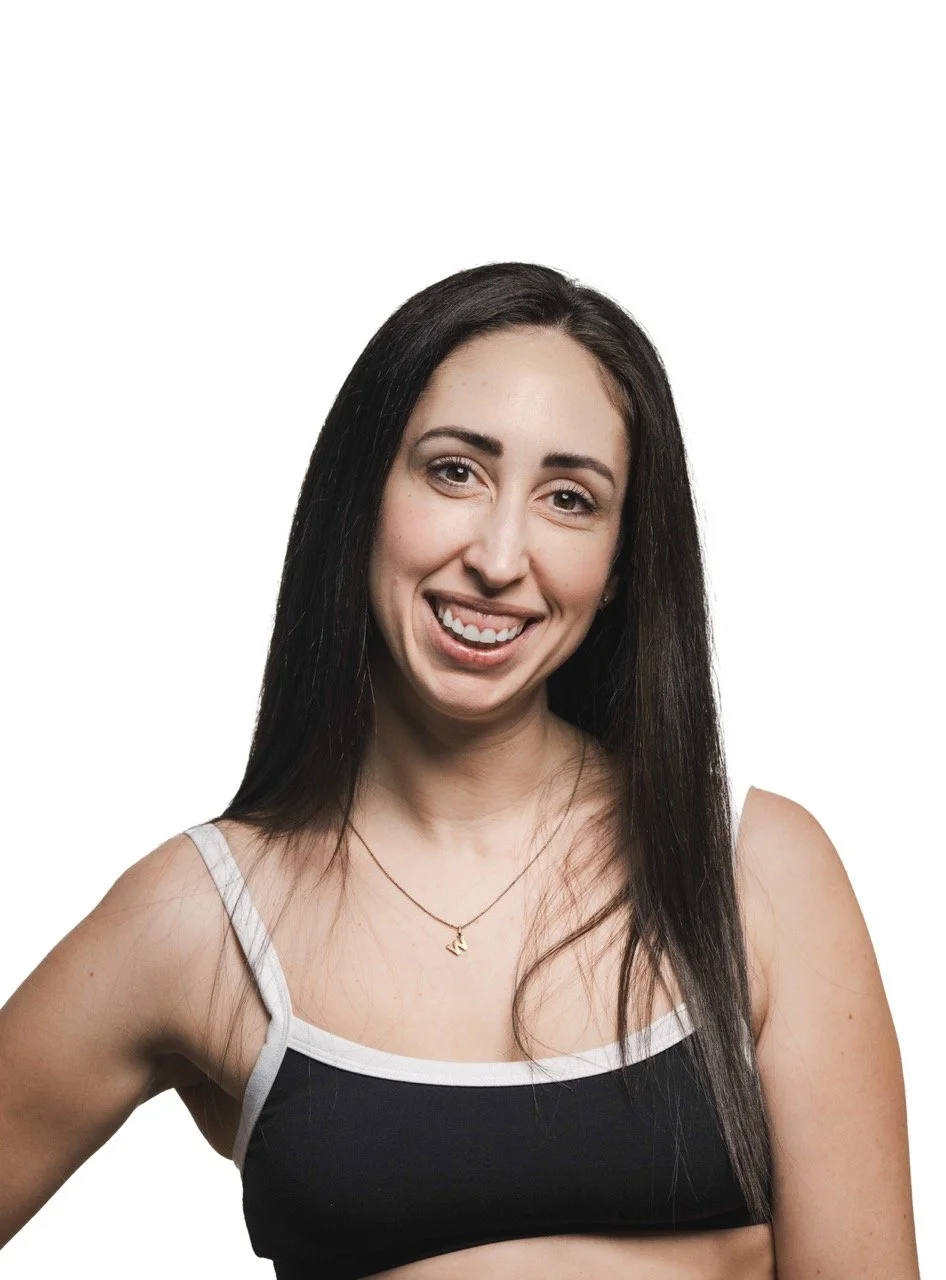 A woman with long dark hair wearing a black crop top with white trim, smiling and winking at the camera, isolated on a white background.