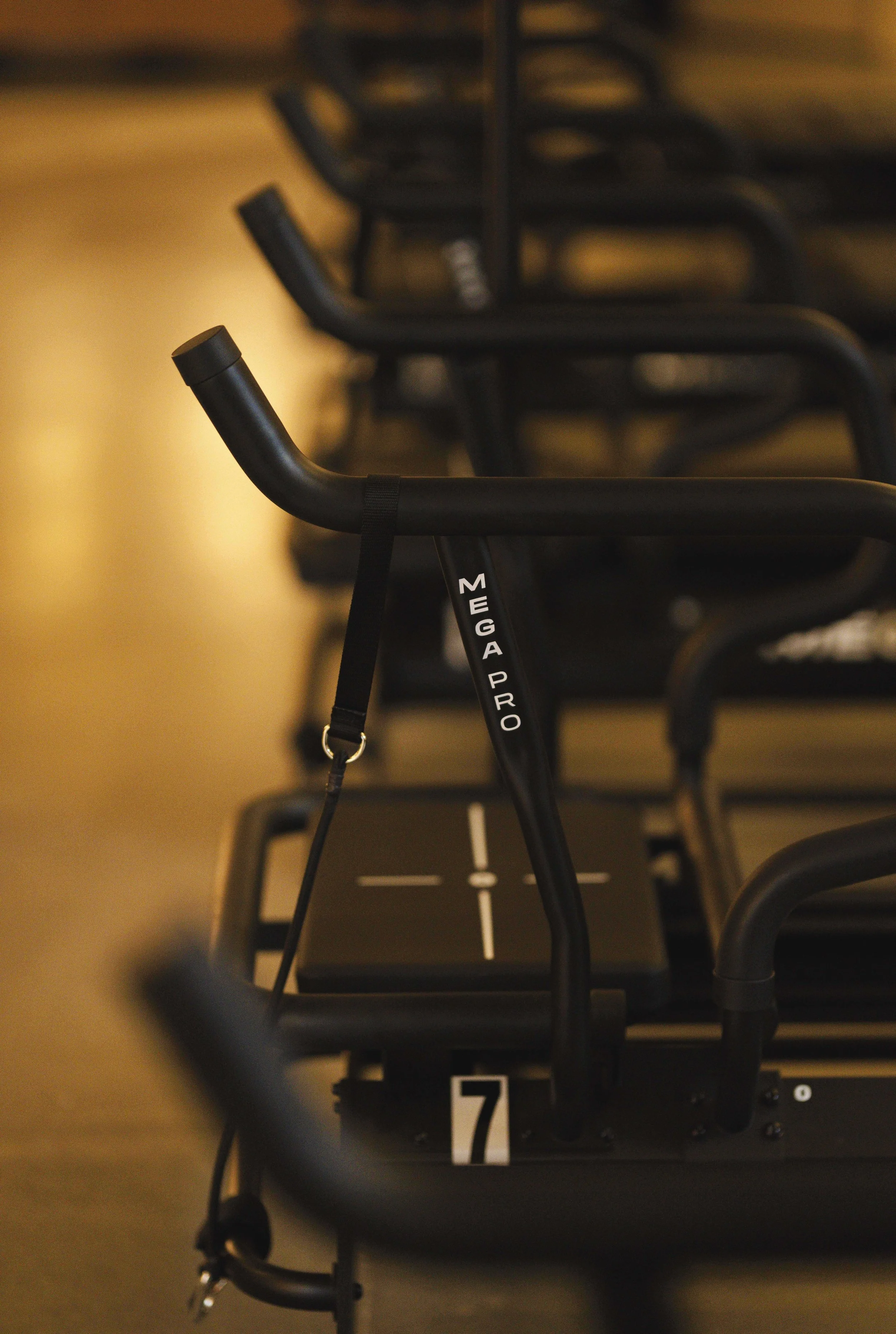 A row of black scooters or kick bikes lined up indoors, with a close-up of one scooter labeled 'MegaPro' in sharp focus and the others blurred in the background.