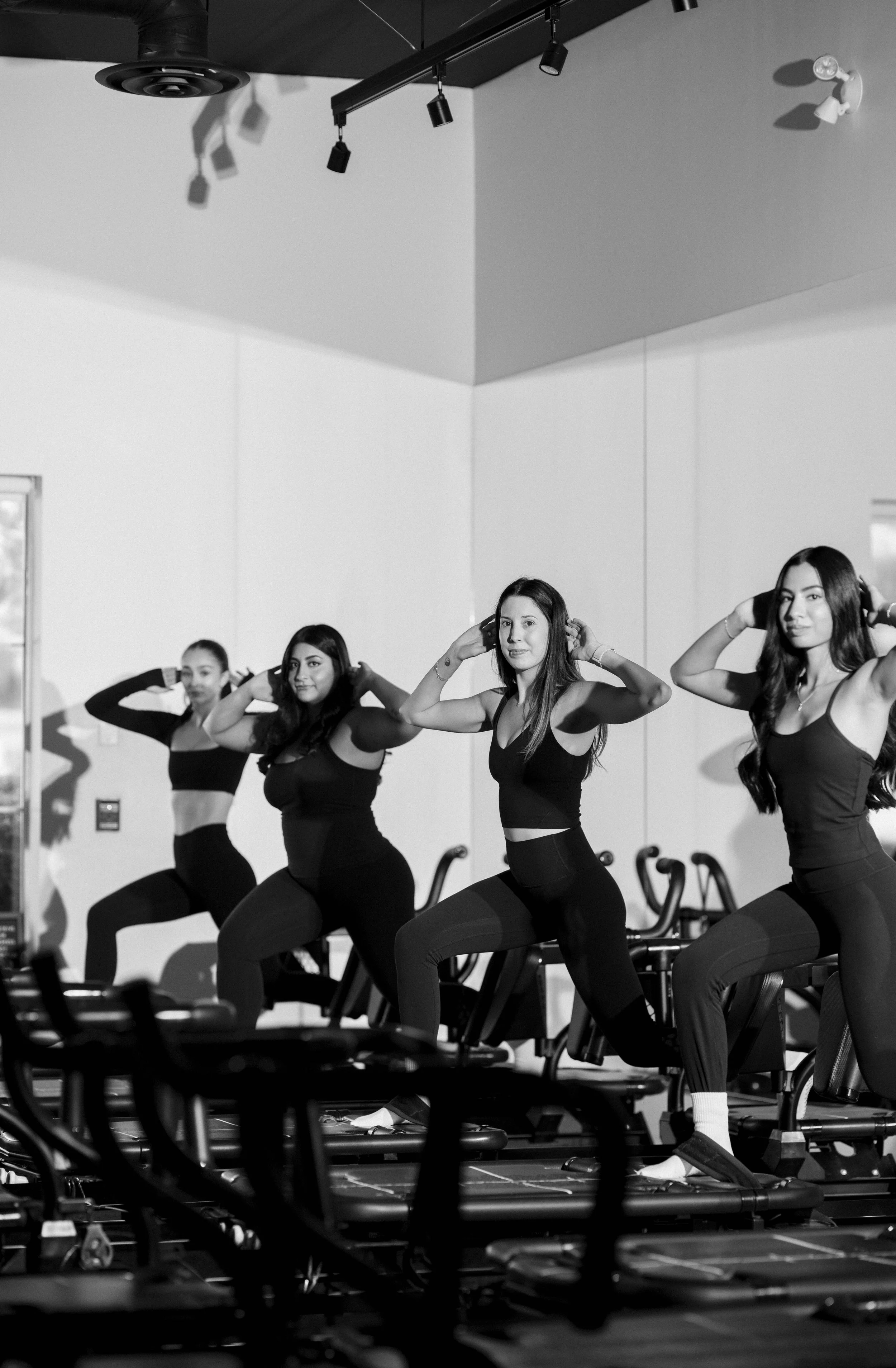 Four women in workout attire doing step aerobics in a gym, wearing headphones.