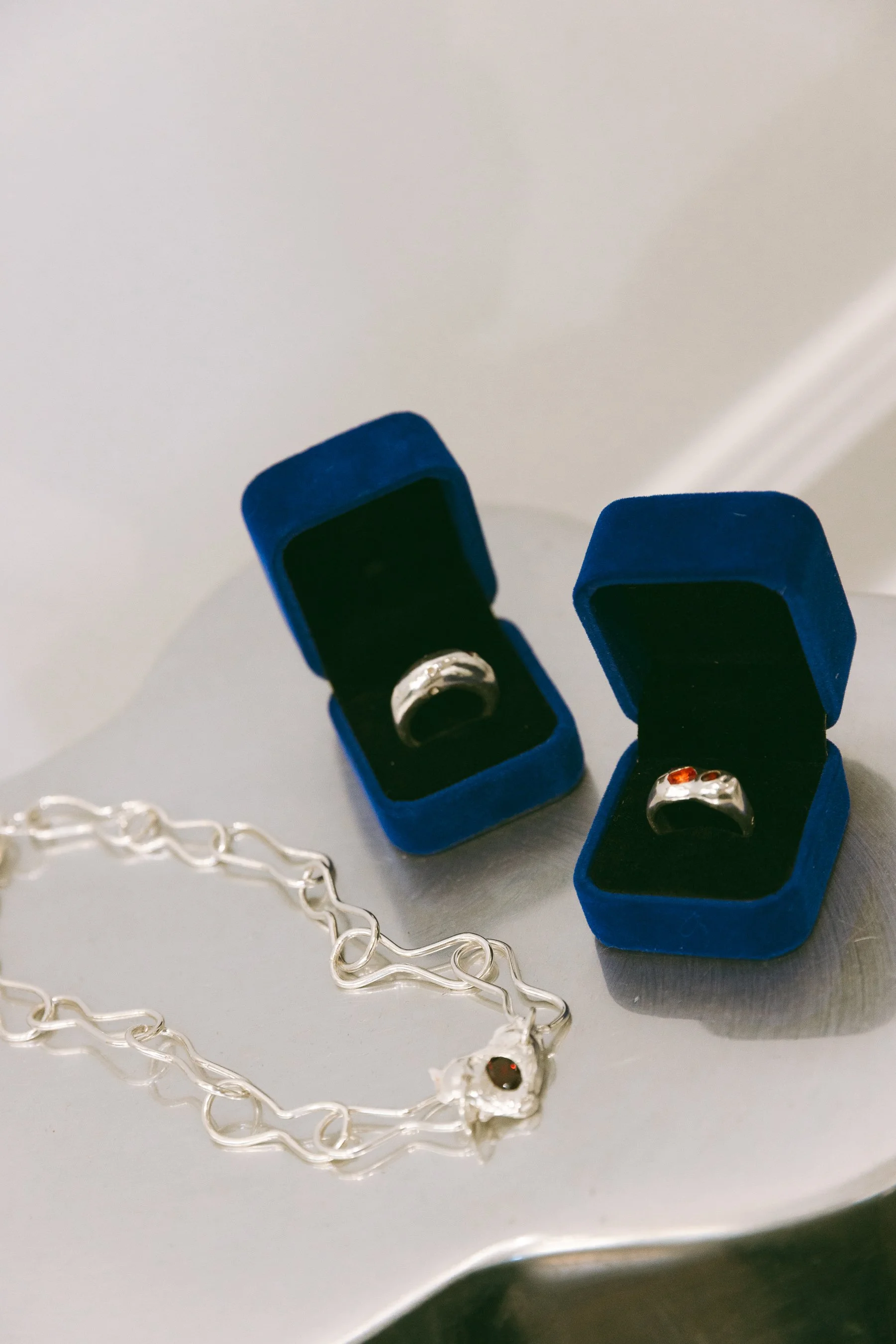 Silver jewelry, including a bracelet and two rings in blue velvet boxes, displayed on a reflective surface.