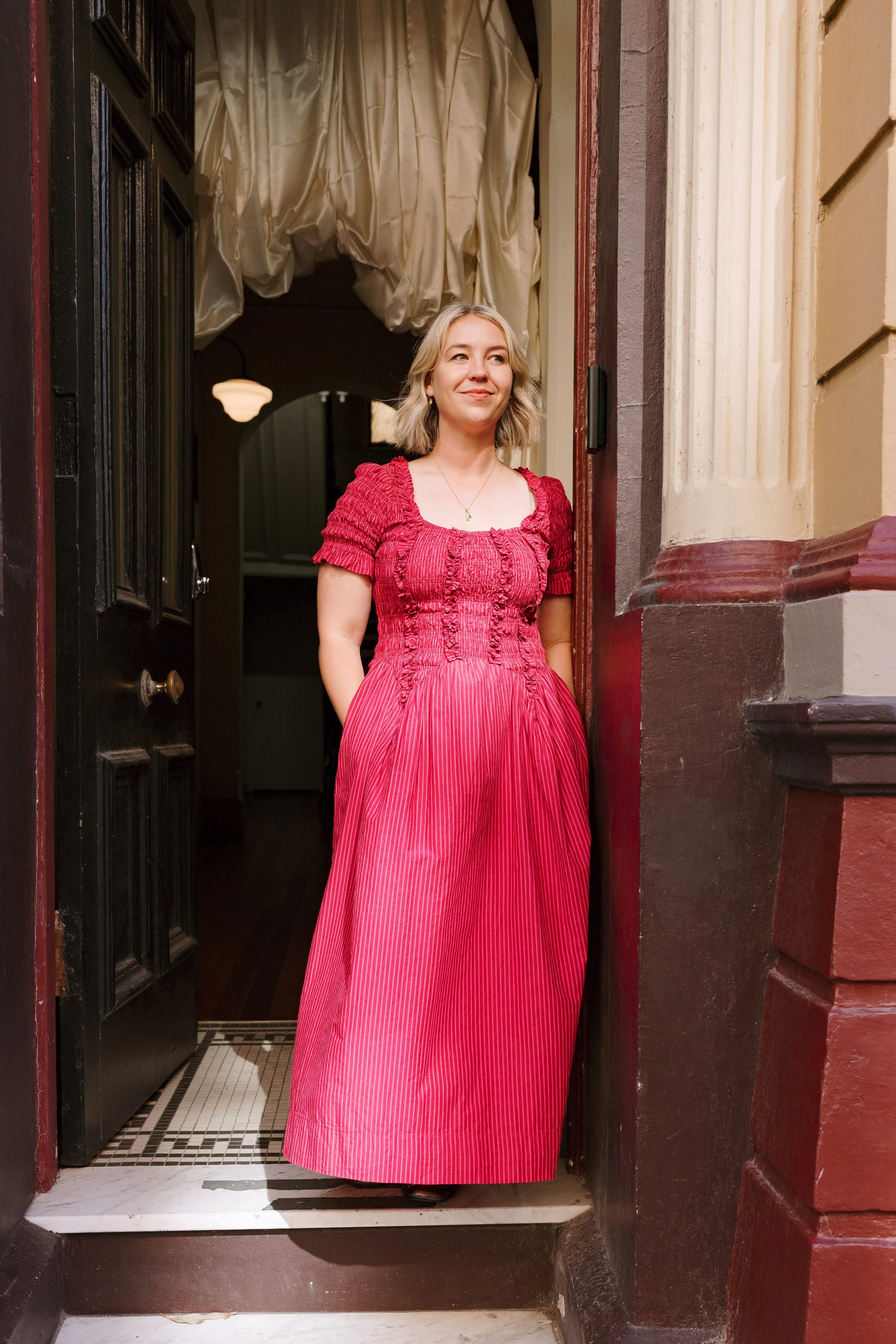 A woman in a pink dress standing in a doorway, smiling.