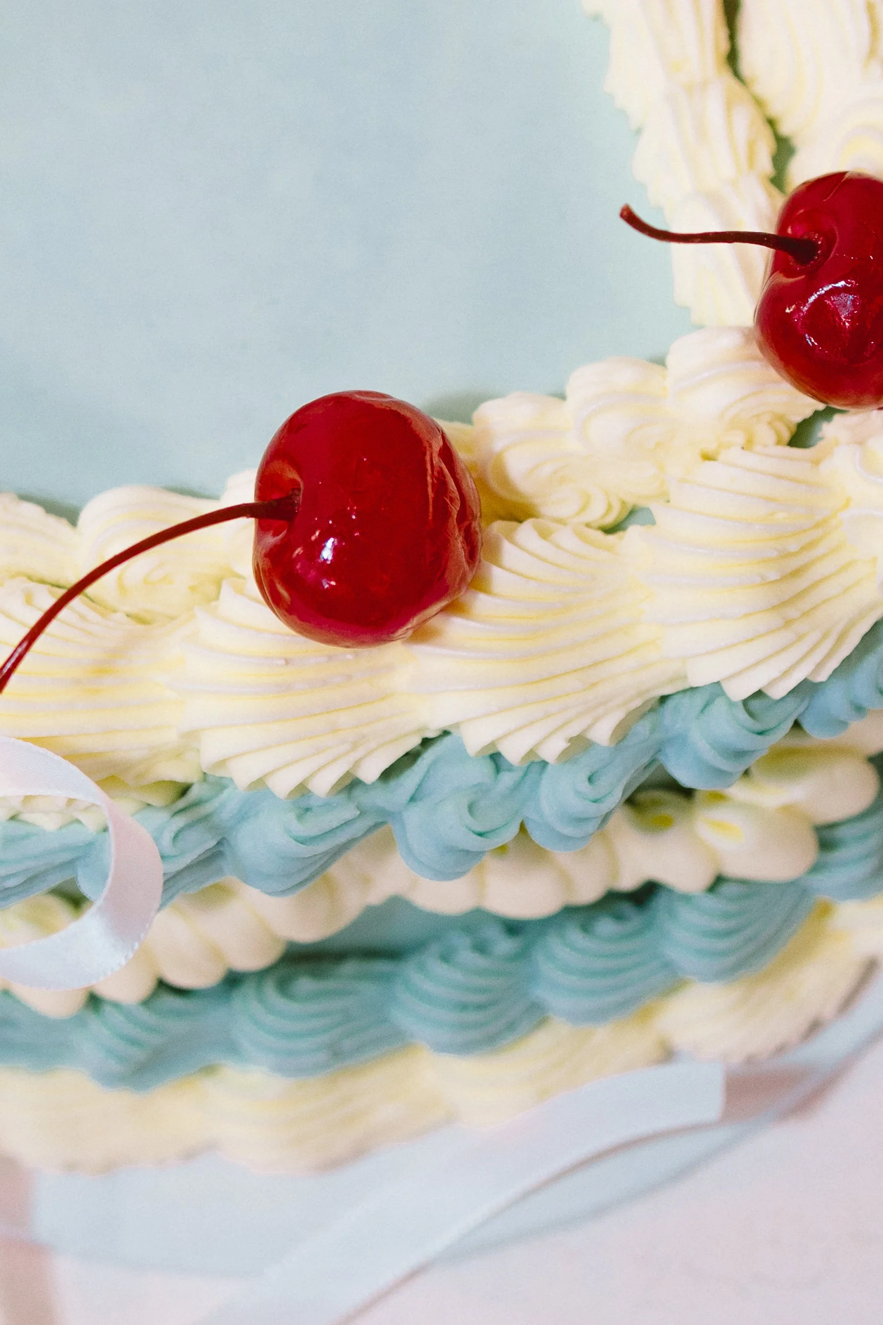 Close-up of a decorated birthday cake with white and blue icing and cherries on top.