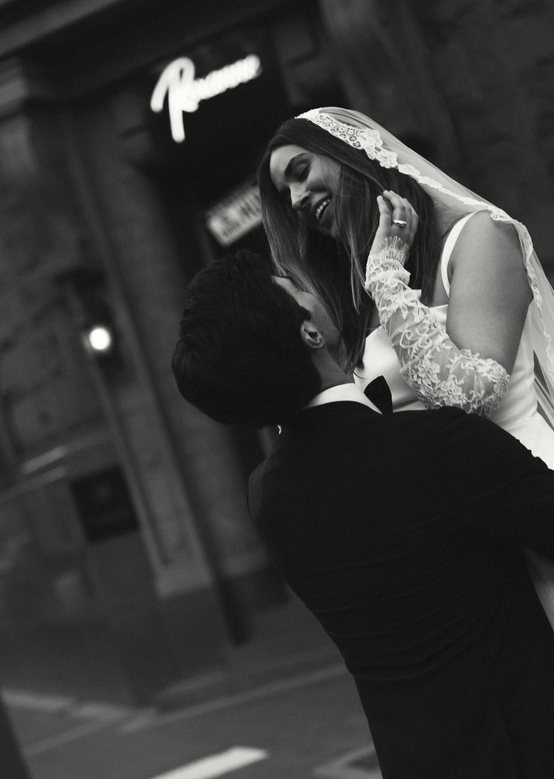 A bride and groom sharing a dance, smiling at each other, during their wedding reception in a black and white photo.