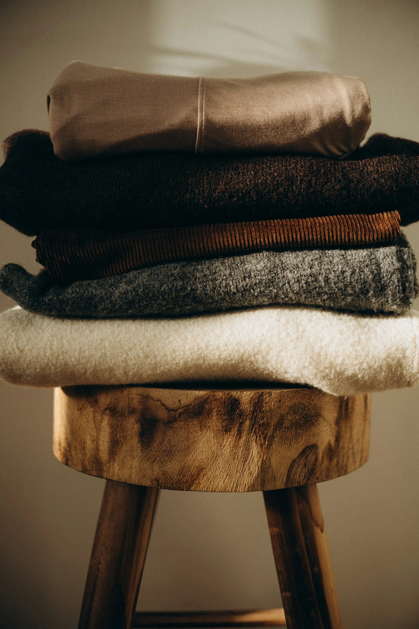 A stack of folded sweaters on a wooden stool.