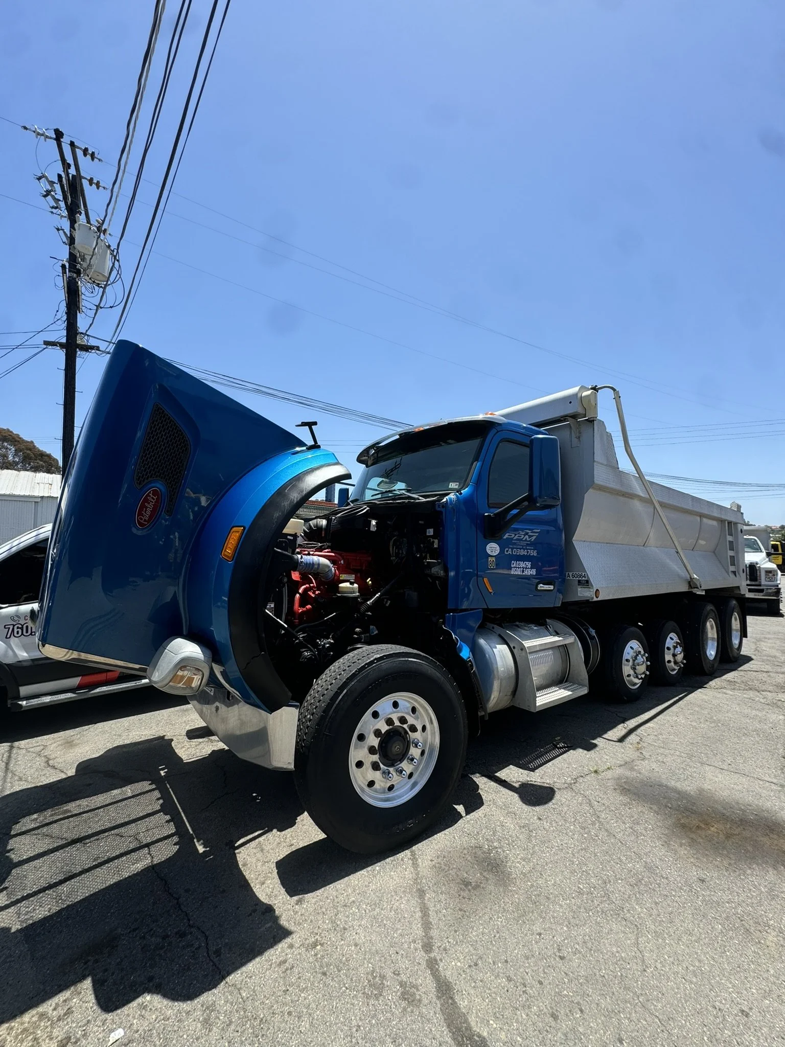 A blue semi-truck with an open hood parked outdoors, showing the engine.