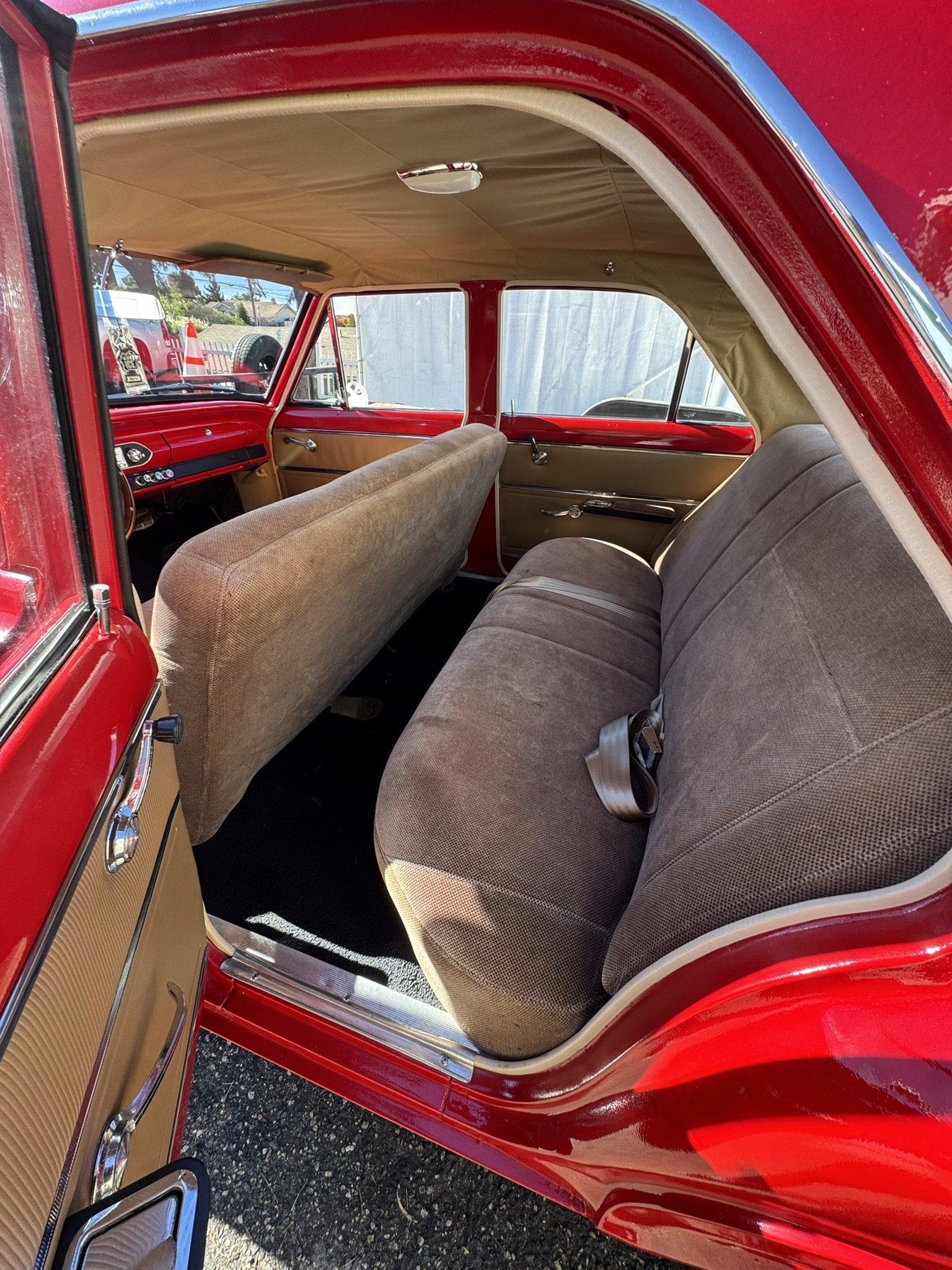 Interior of a vintage red car showing beige and brown seats, beige door panels, and a grab handle.